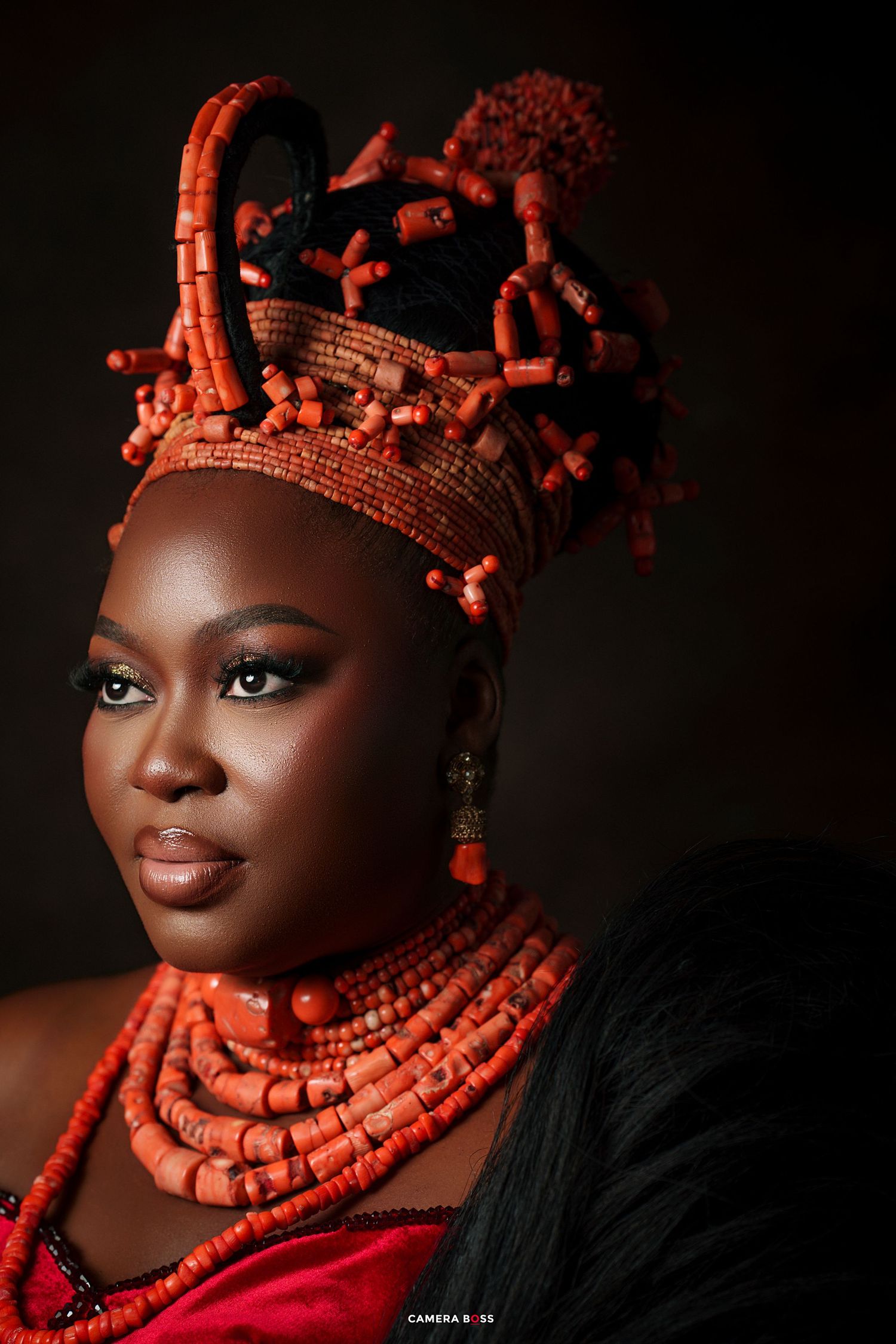 Woman wearing traditional Nigerian coral beaded crown and necklaces in red and orange, dressed in ceremonial attire.