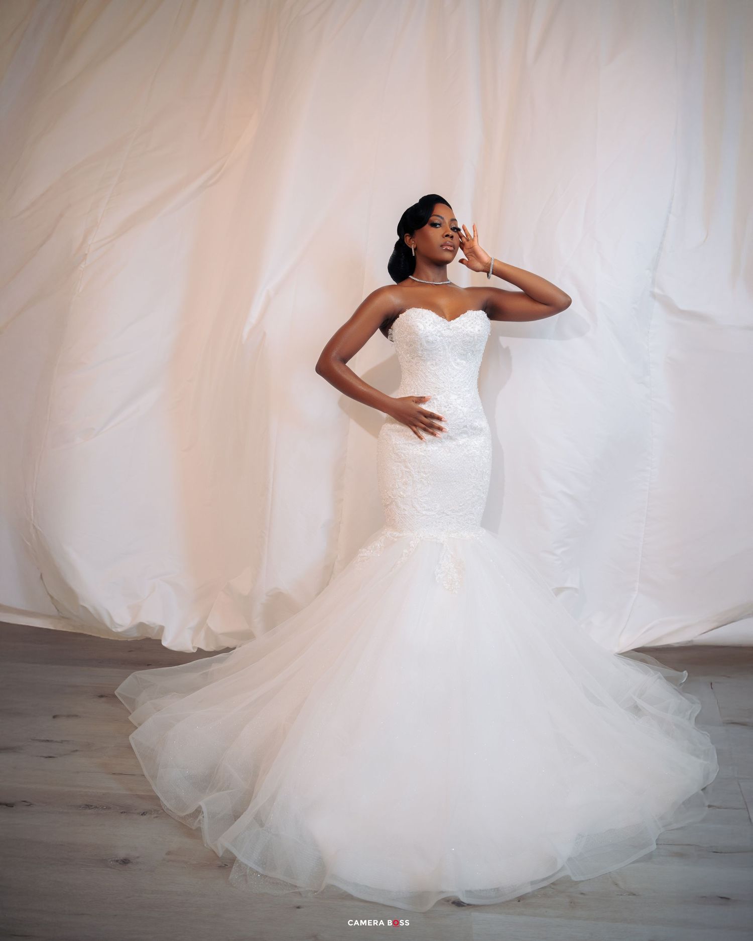 A bride in a stunning white strapless mermaid wedding gown poses elegantly against a flowing white backdrop.