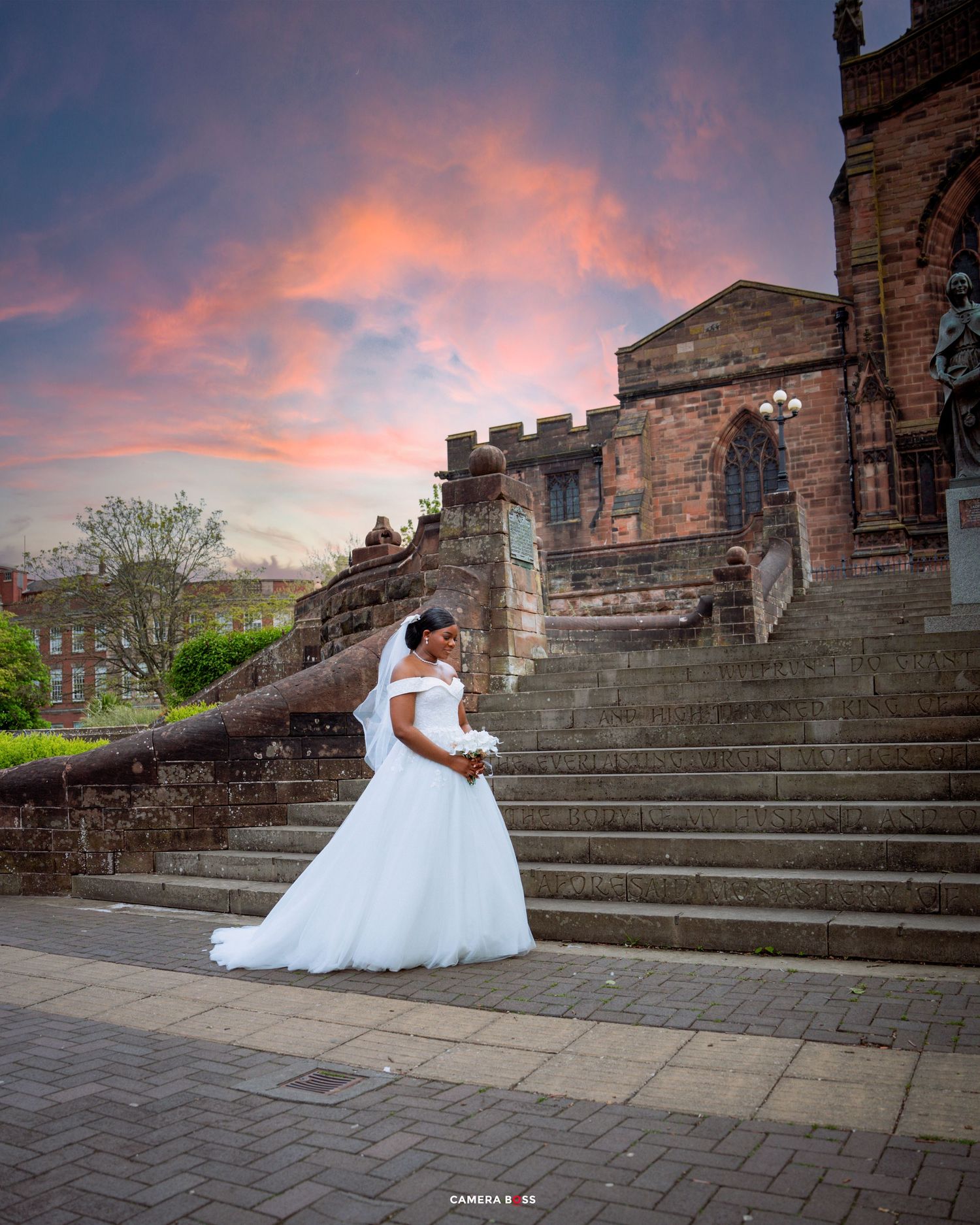 A wedding dress silhouette on dramatic stone steps of a historic church with stunning orange and purple sunset skies.