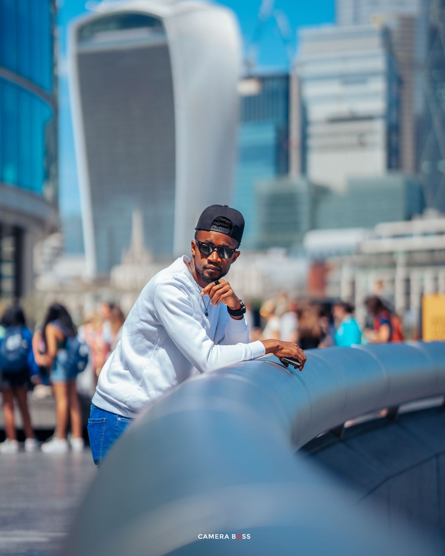 Person in white sweater and cap poses against urban backdrop with London's iconic Walkie Talkie building visible.