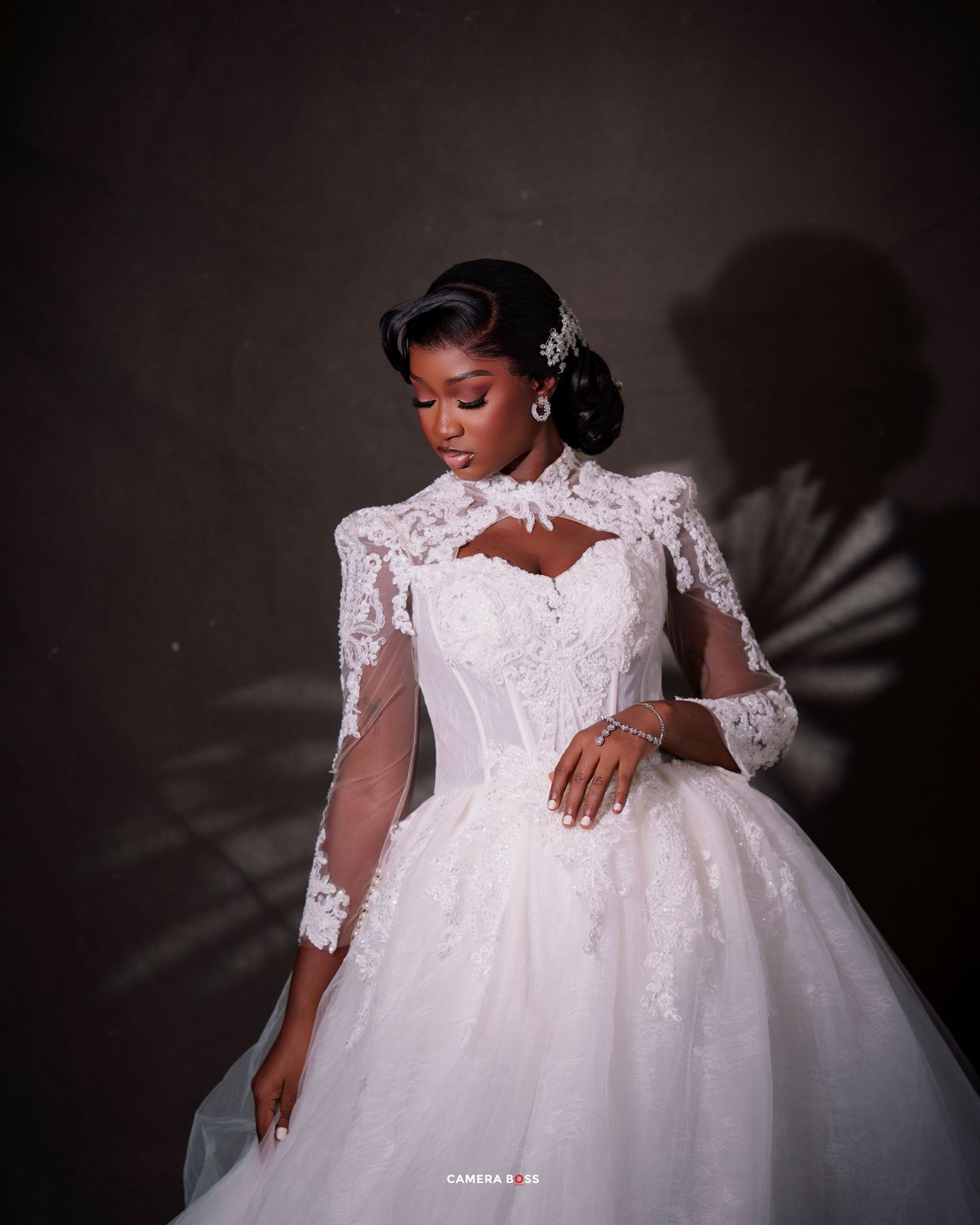 Elegant bride in white lace ball gown with long sleeves and floral hair accessory, posing gracefully.