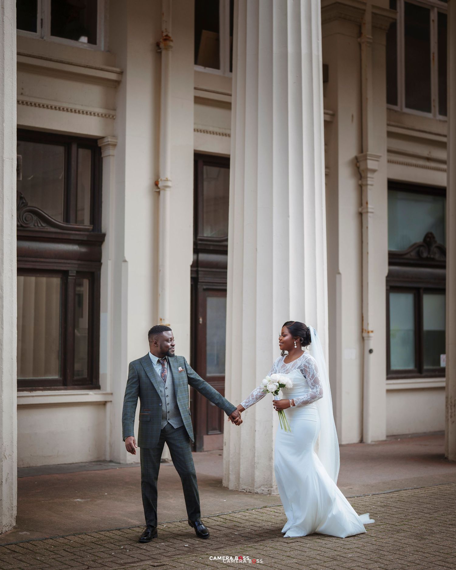 Bride and groom holding hands in front of grand white columns during outdoor wedding photo session.
