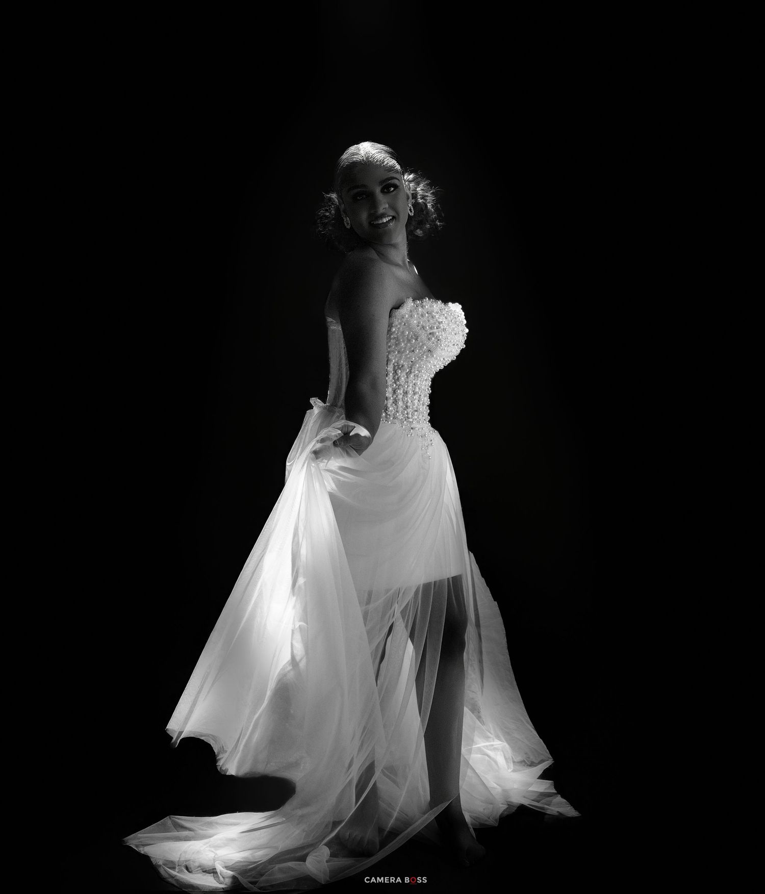Elegant bride in a white strapless gown poses gracefully in a dramatic black and white studio portrait.