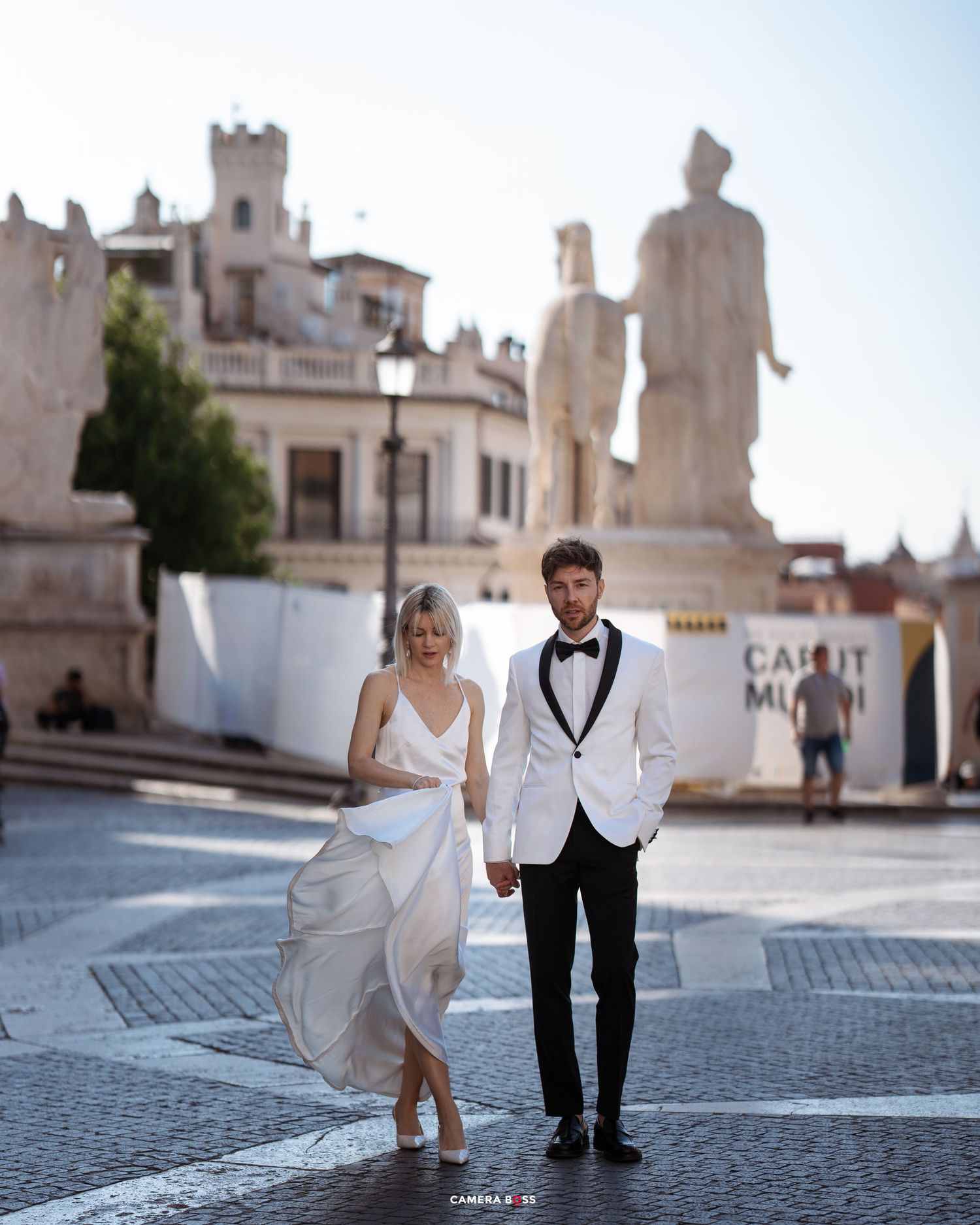 A minimalist artistic photoset of two people in wedding attire posing on cobblestone steps in front of a white building.