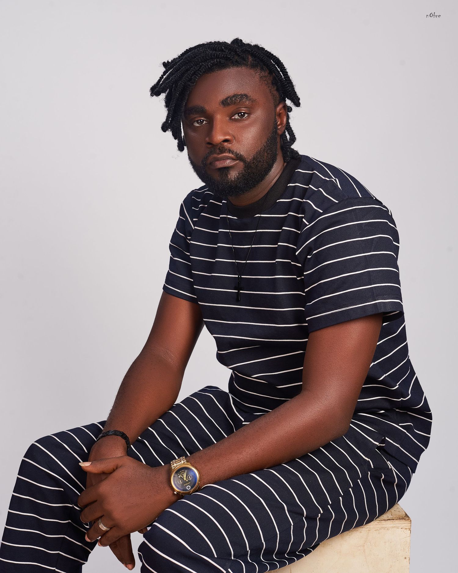 Person in black and white striped loungewear outfit sitting on beige surface against light background.