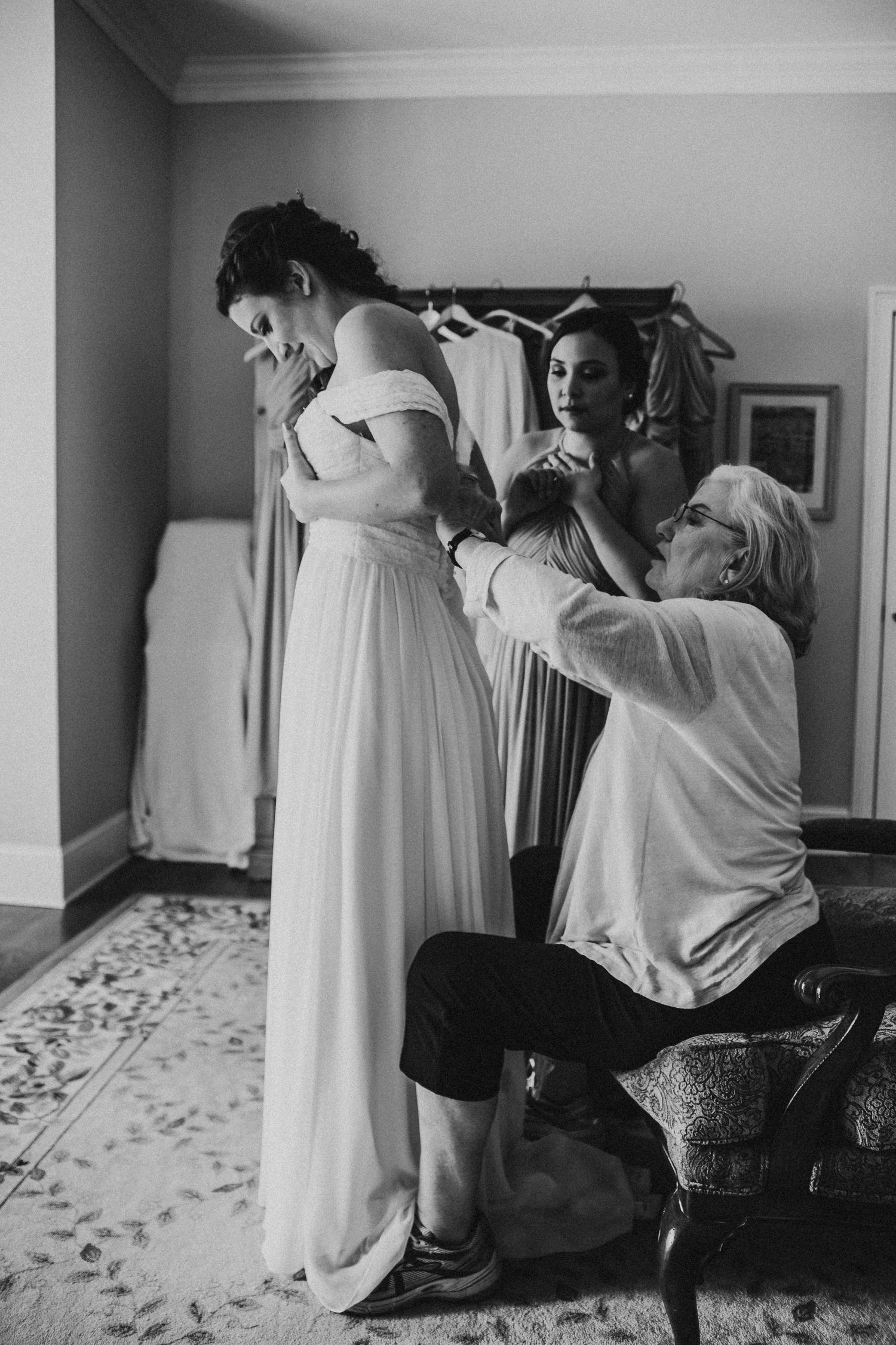 Mother of the bride helping her daughter get her dress buttoned up in black and white
