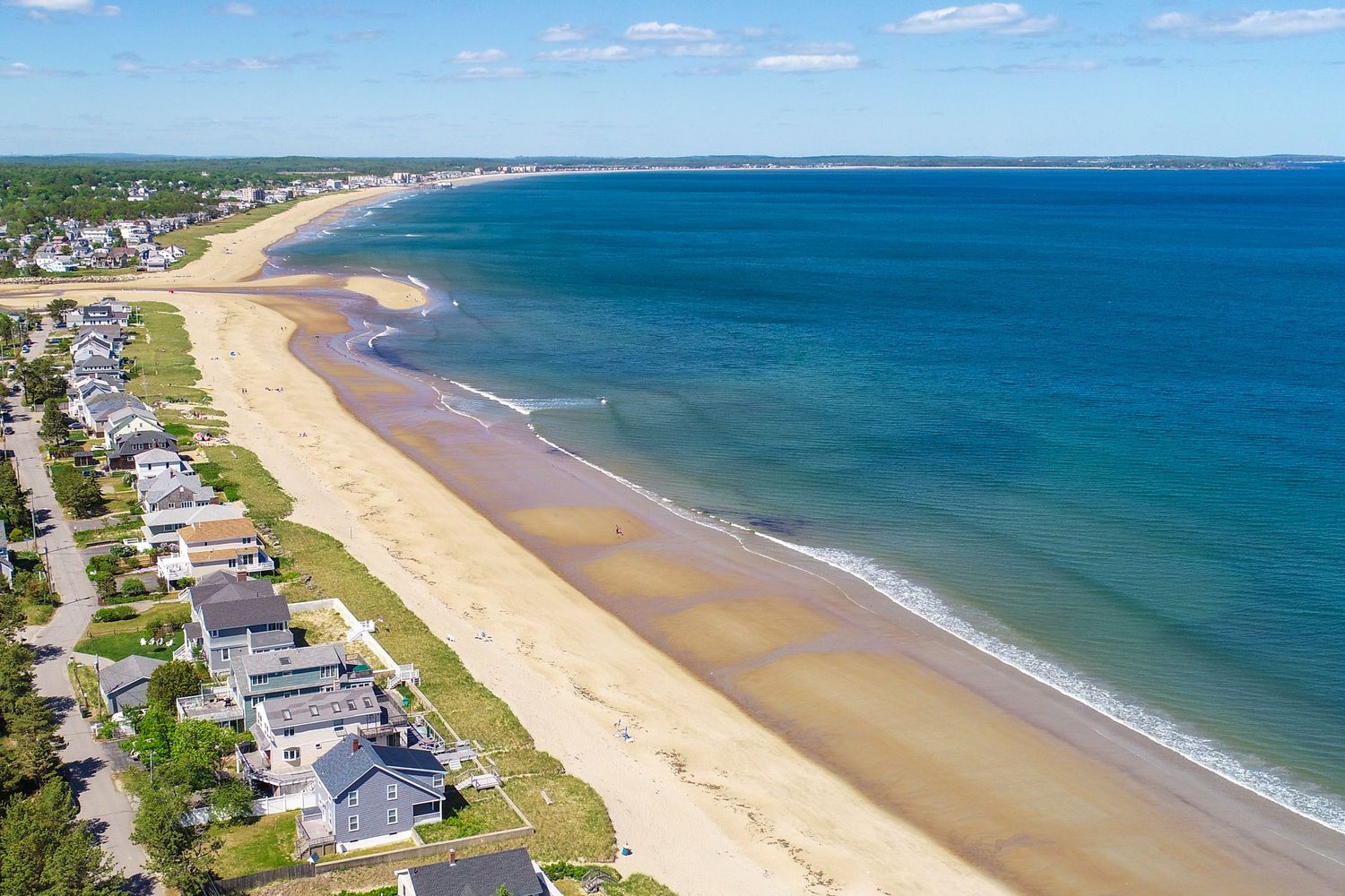 Aerial view of a sandy beach with turquoise ocean waters, beachfront homes, and a clear blue sky on a sunny day.