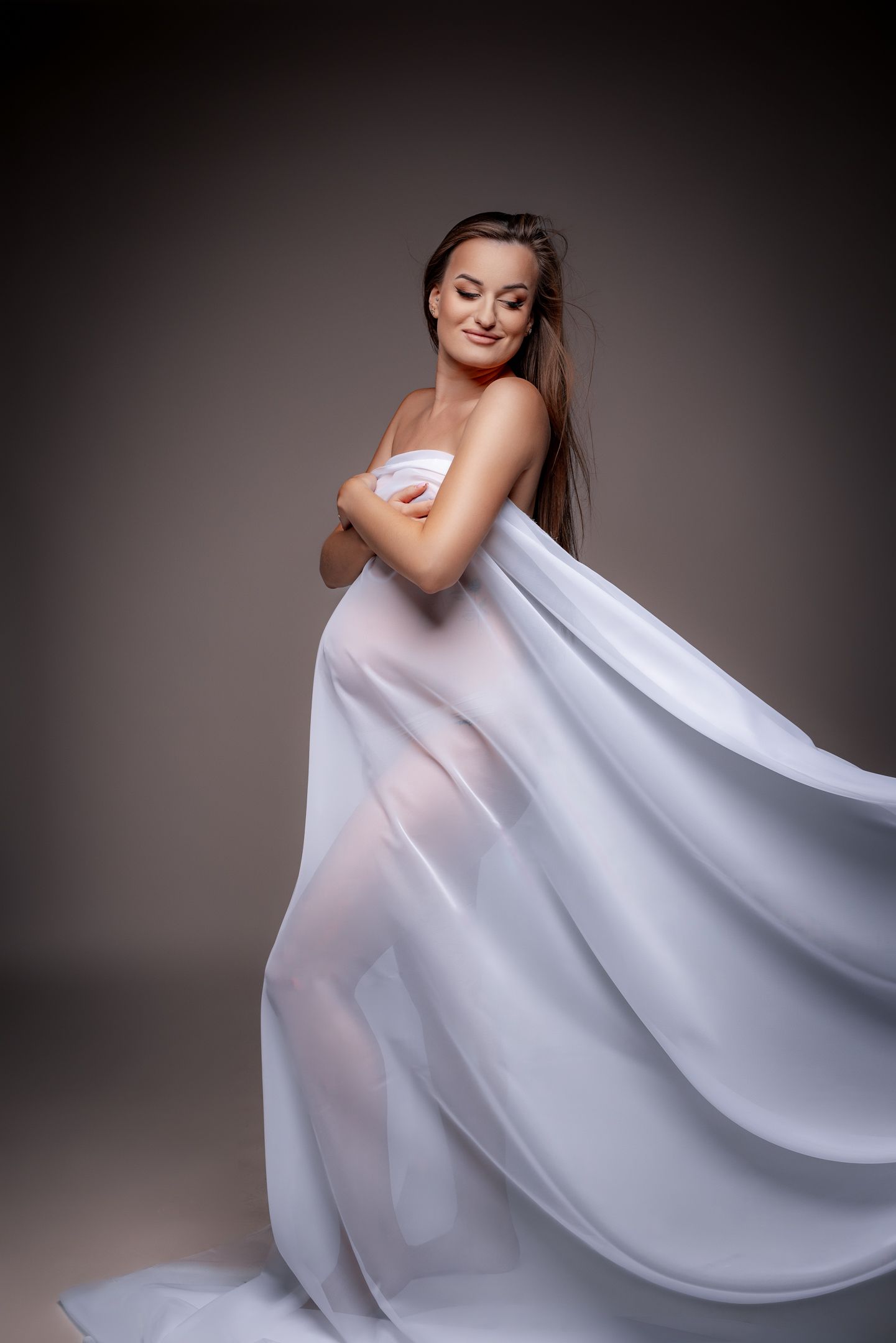 Artistic boudoir photo with flowing white fabric in studio lighting against dark background.