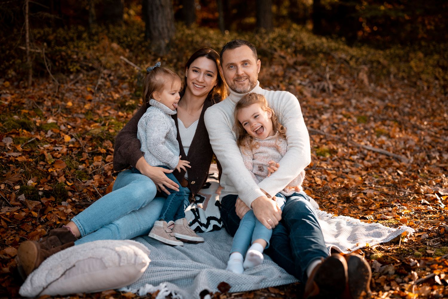 Autumn family portrait on blanket with fallen leaves and warm lighting.
