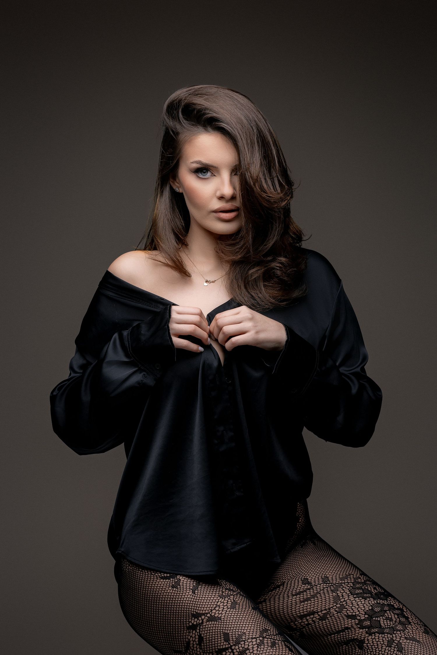 Dramatic studio portrait in black silk blouse against dark background.