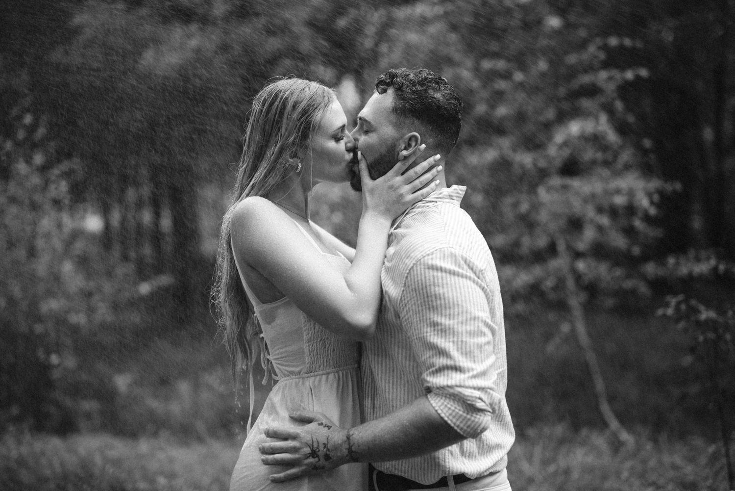 A romantic black and white photograph of an intimate couple sharing a tender kiss outdoors.