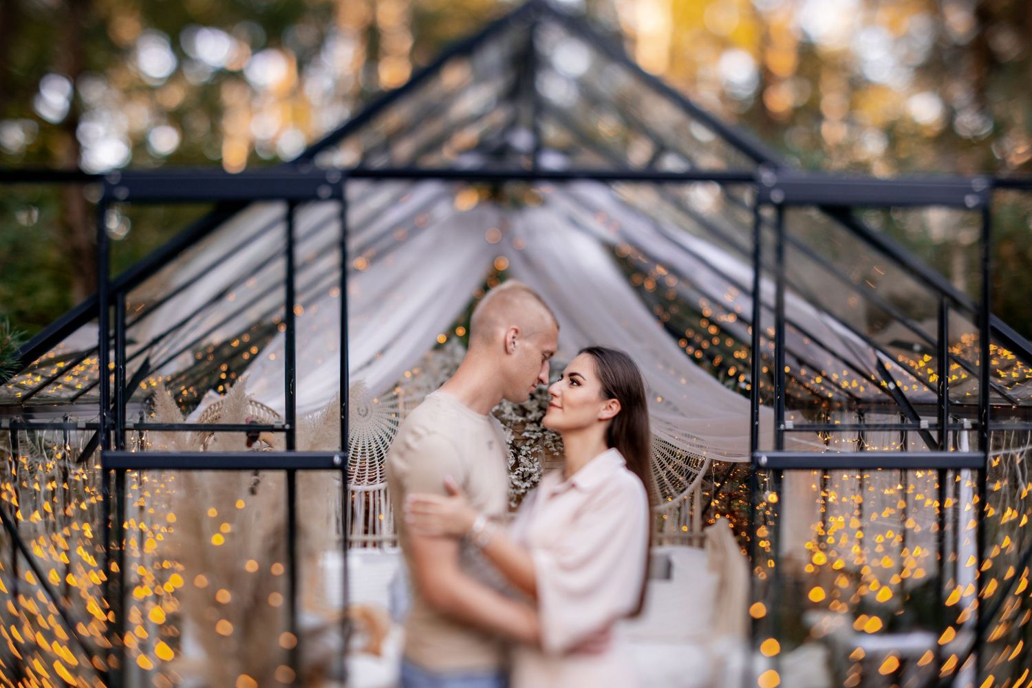 Romantic moment captured in greenhouse with fairy lights and soft focus.