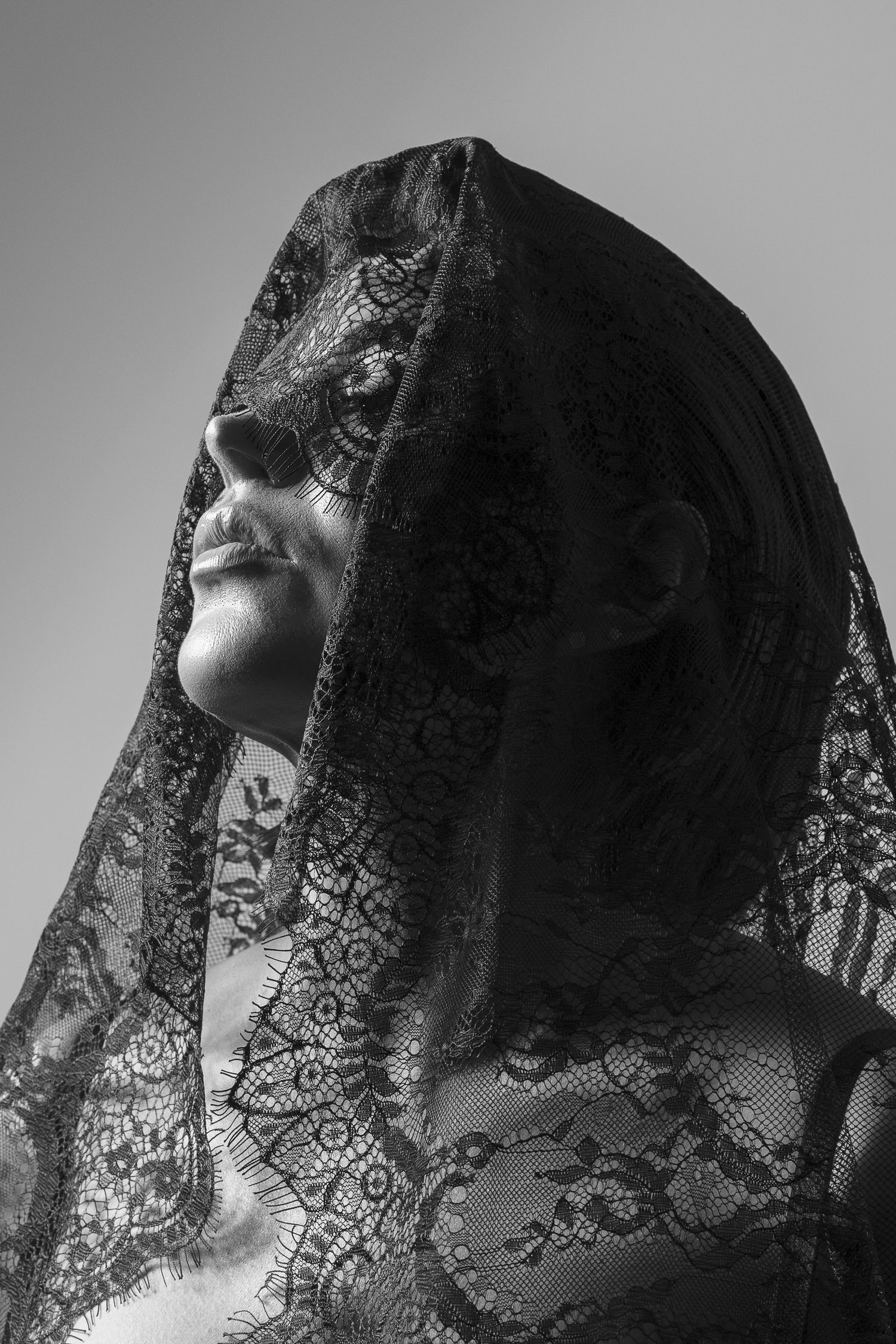 Black and white portrait of woman with lace veil covering face, moody fine art photography.