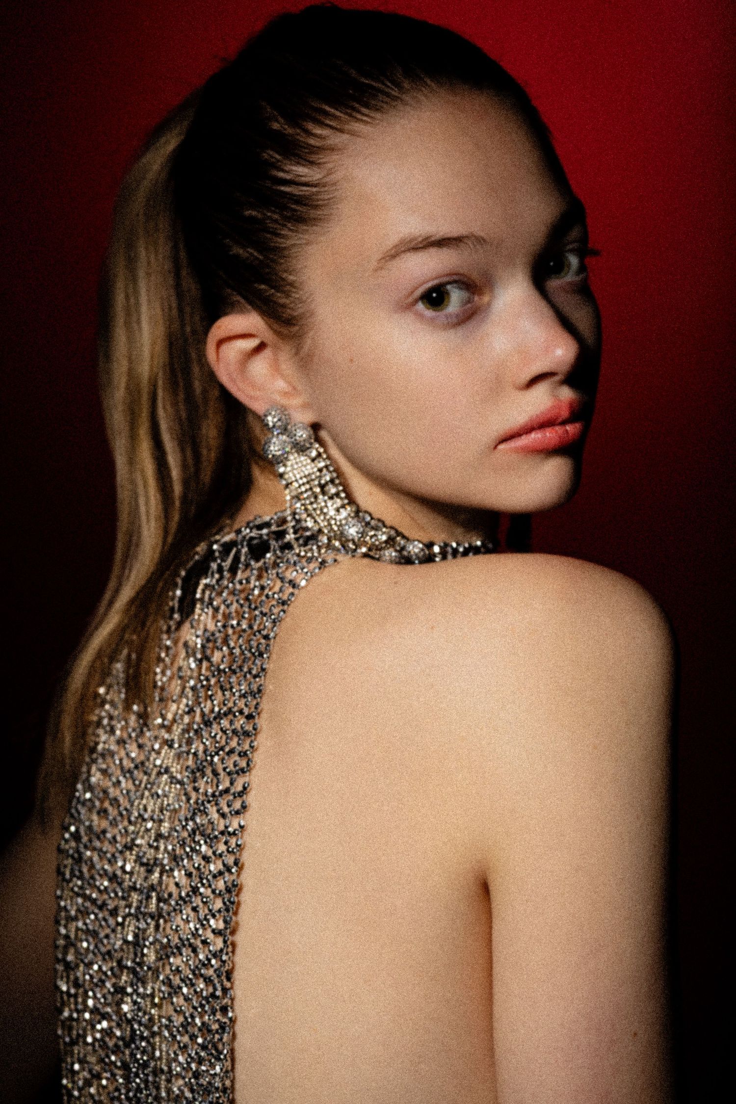 Close-up beauty portrait of woman with statement jewelry against red background, bold lighting editorial style. Girl with the pearl earing