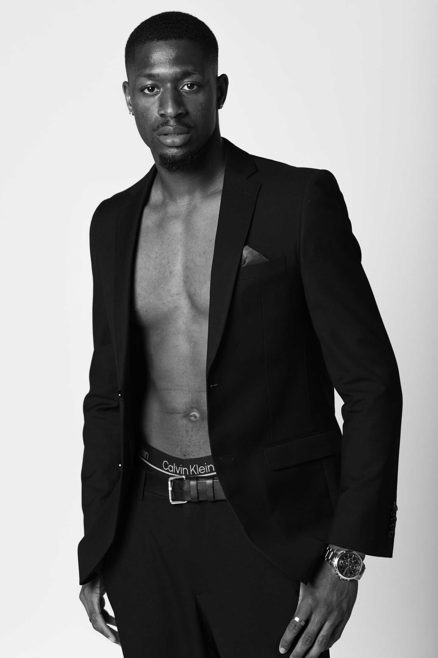 Confident Black male model in open black blazer showing muscular torso, professional studio portrait, fashion photography