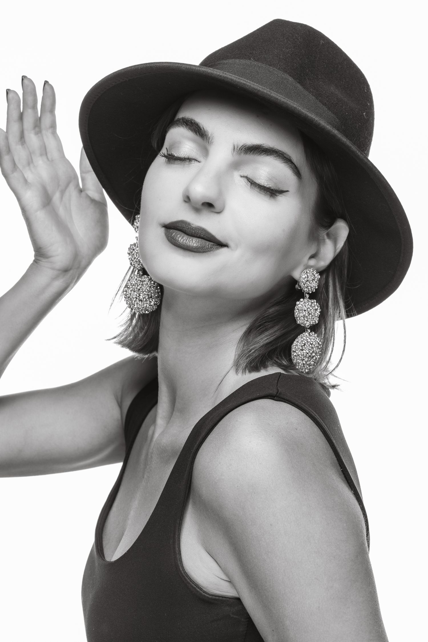 Stylish woman in wide-brim fedora hat with closed eyes and raised hand, elegant black and white fashion portrait