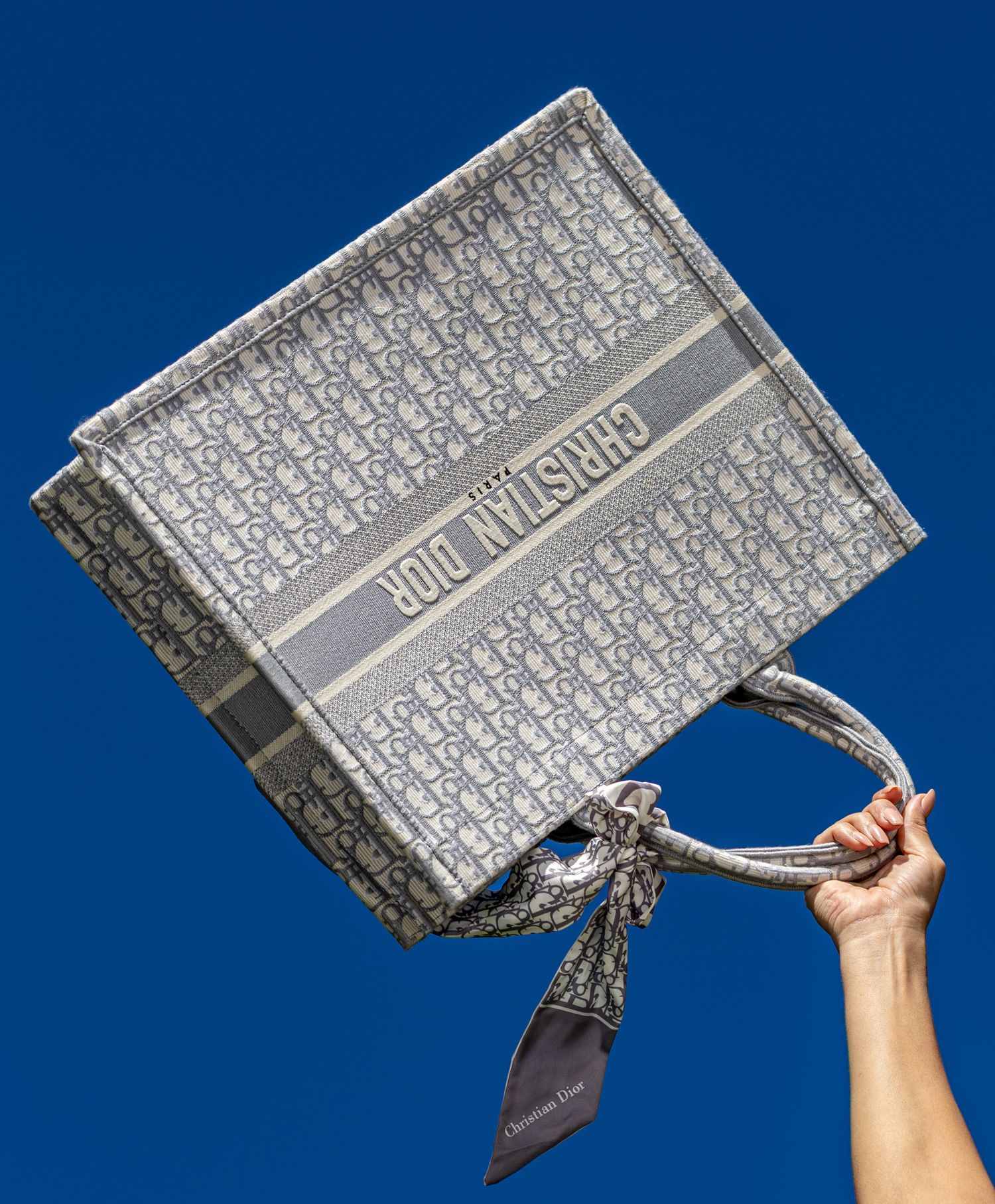Designer Dior book held against bright blue background, minimalist fashion still life with bold contrast and luxury aesthetic.