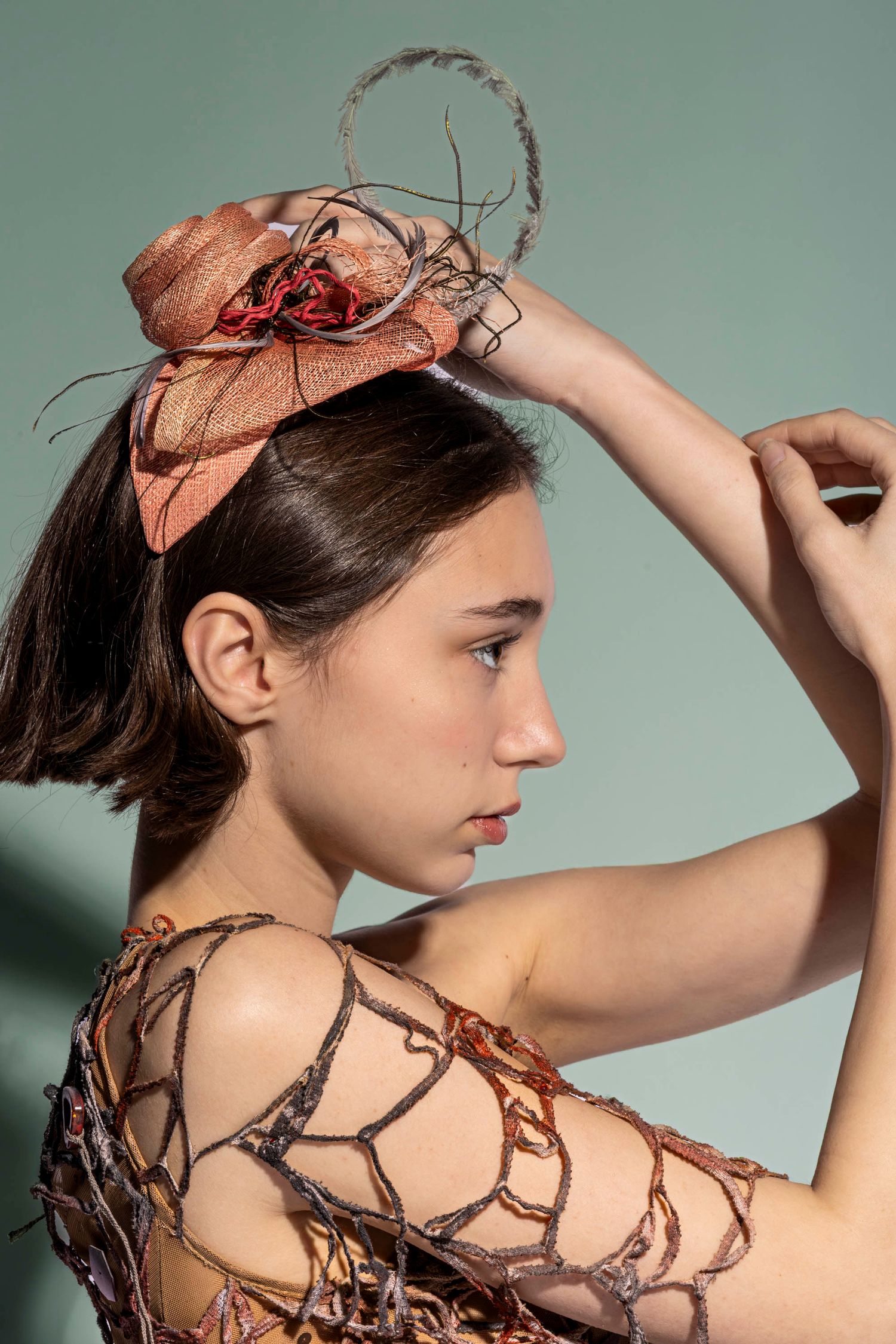Profile portrait of model wearing sculptural headpiece, creative fashion styling with clean background.