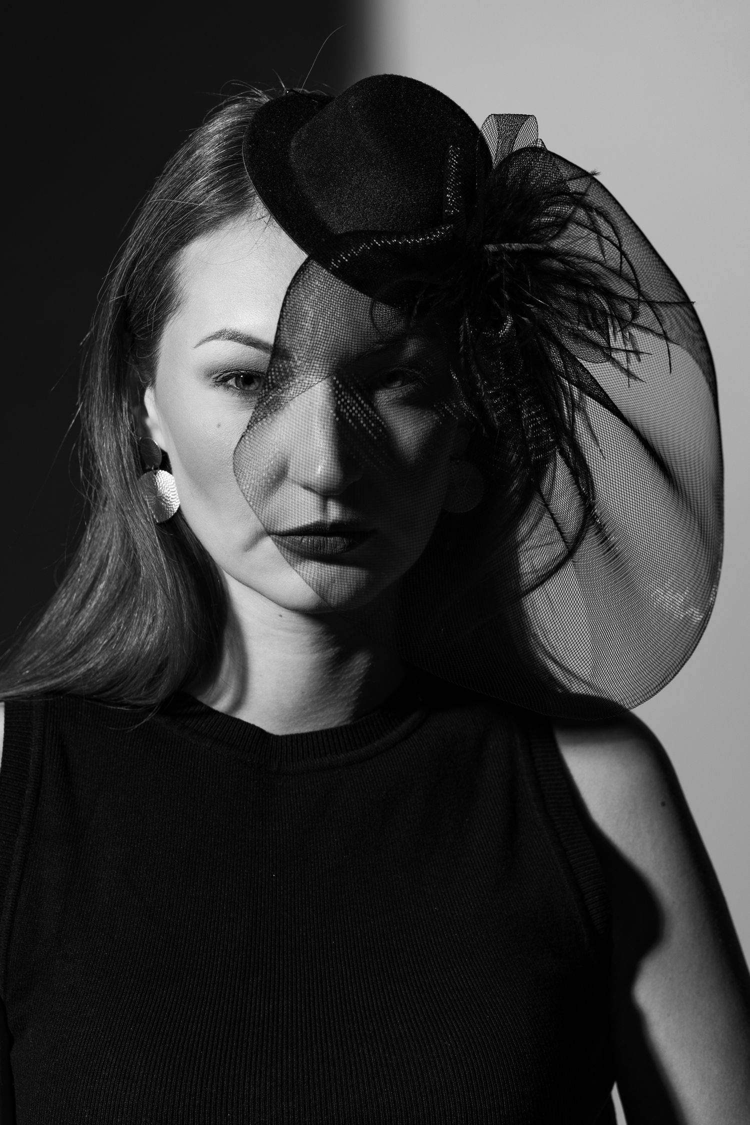 Dramatic woman wearing black fascinator veil and hat, intense gaze, high-fashion studio portrait in monochrome