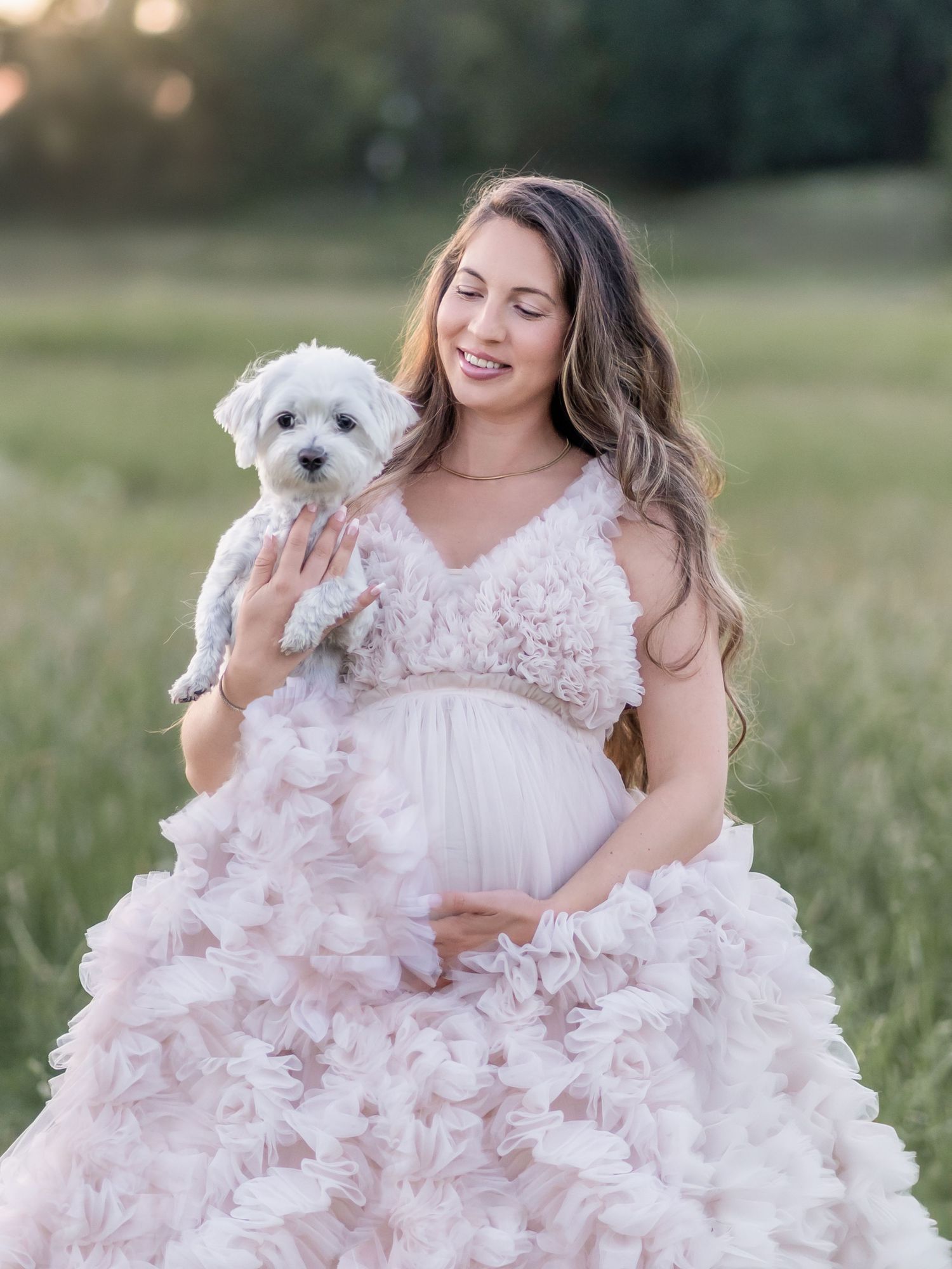 Gravid kvinna i rosa tyllklänning med liten vit hund fotograferad utomhus , gravidfotografering i Stockholm.
