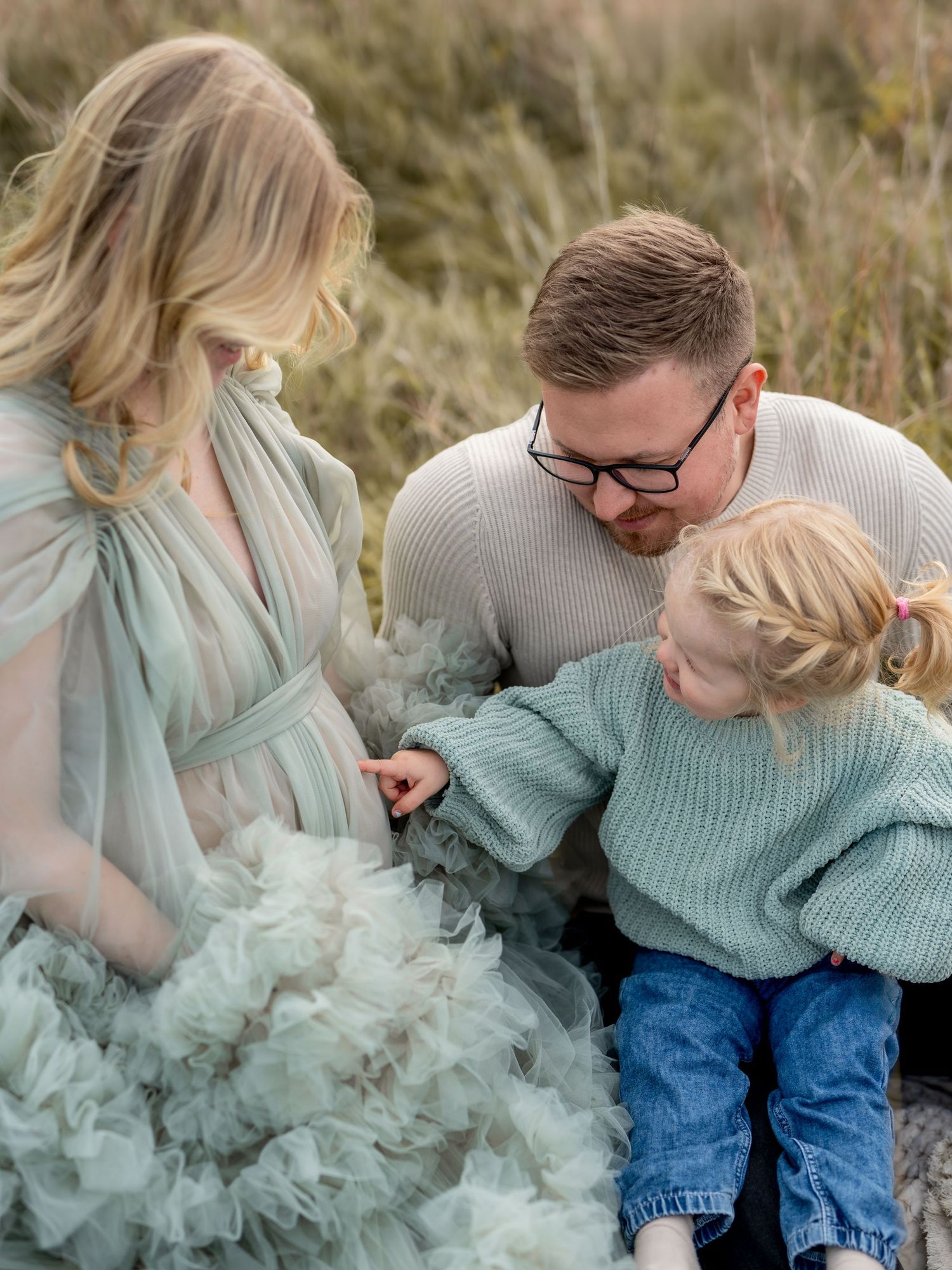 Gravid kvinna i tyllklänning tillsammans med partner och barn fotograferade utomhus. En familjefokuserad gravidfotografering i Stockholm.