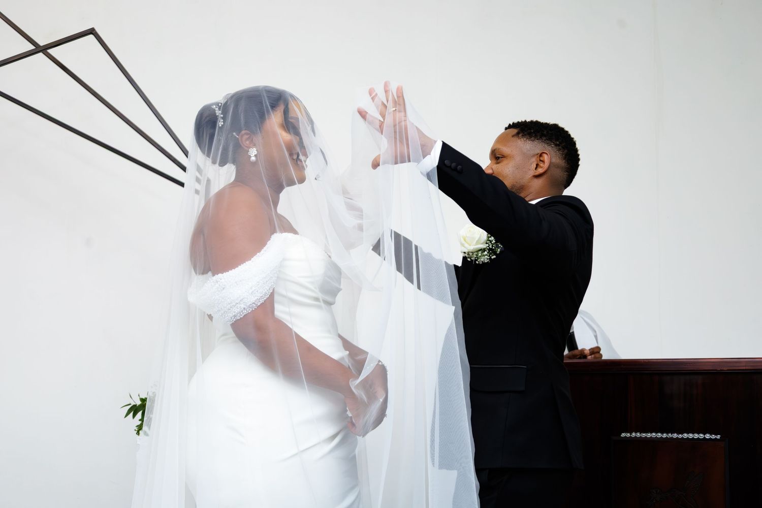 Groom lifts bride's veil during romantic wedding ceremony moment at church altar.