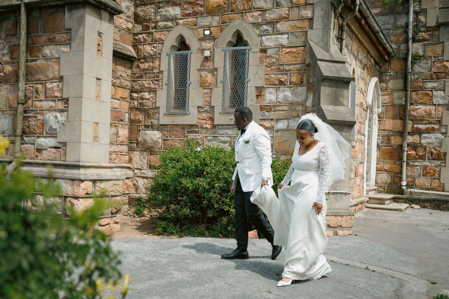 Bride and groom walk outside historic stone church on their wedding day.