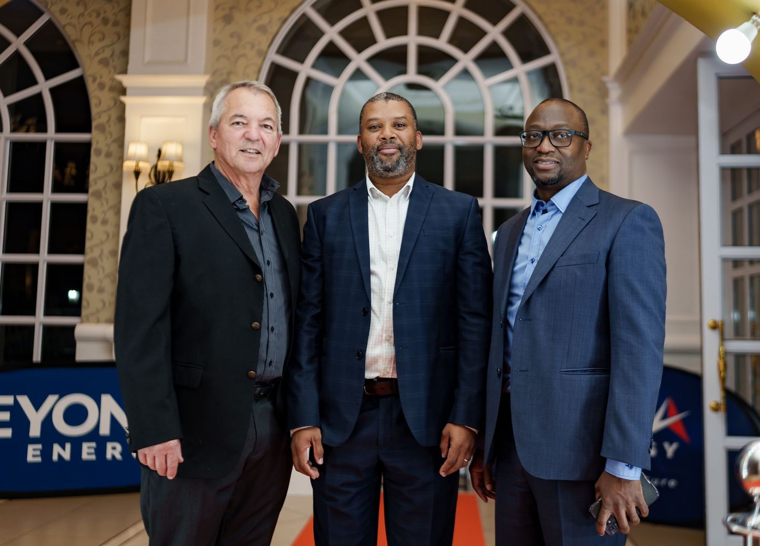 Three men in formal attire posing together at a Beyond Energy corporate event.