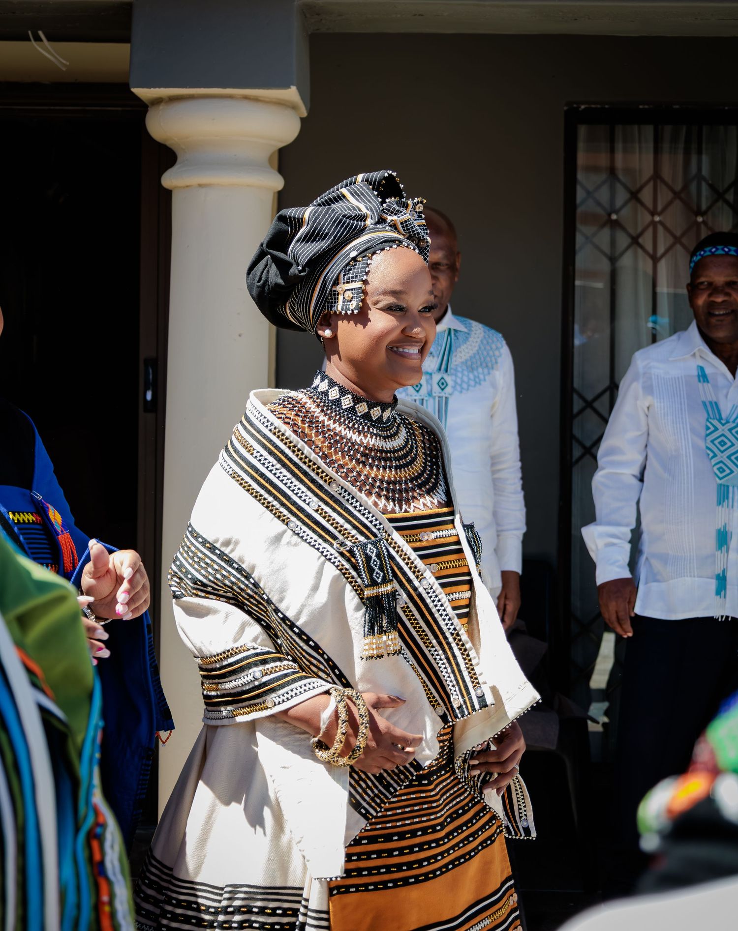 Woman in elegant traditional Xhosa beaded attire and headwrap smiles at a cultural ceremony.