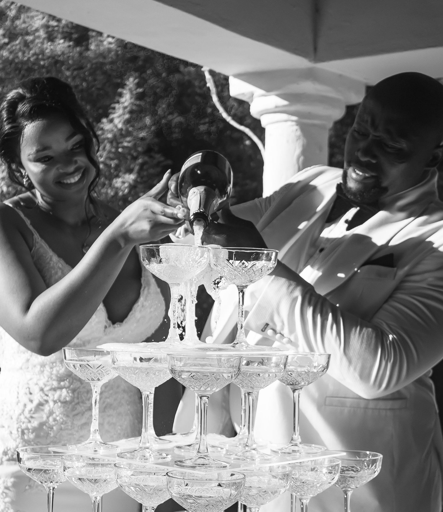 Bride and groom joyfully pouring champagne over a crystal tower of glasses at their wedding reception.