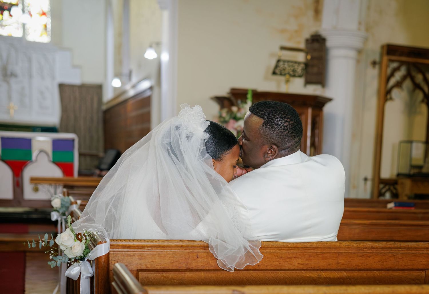 Bride and groom sharing an intimate embrace on a wooden church pew during their wedding ceremony.