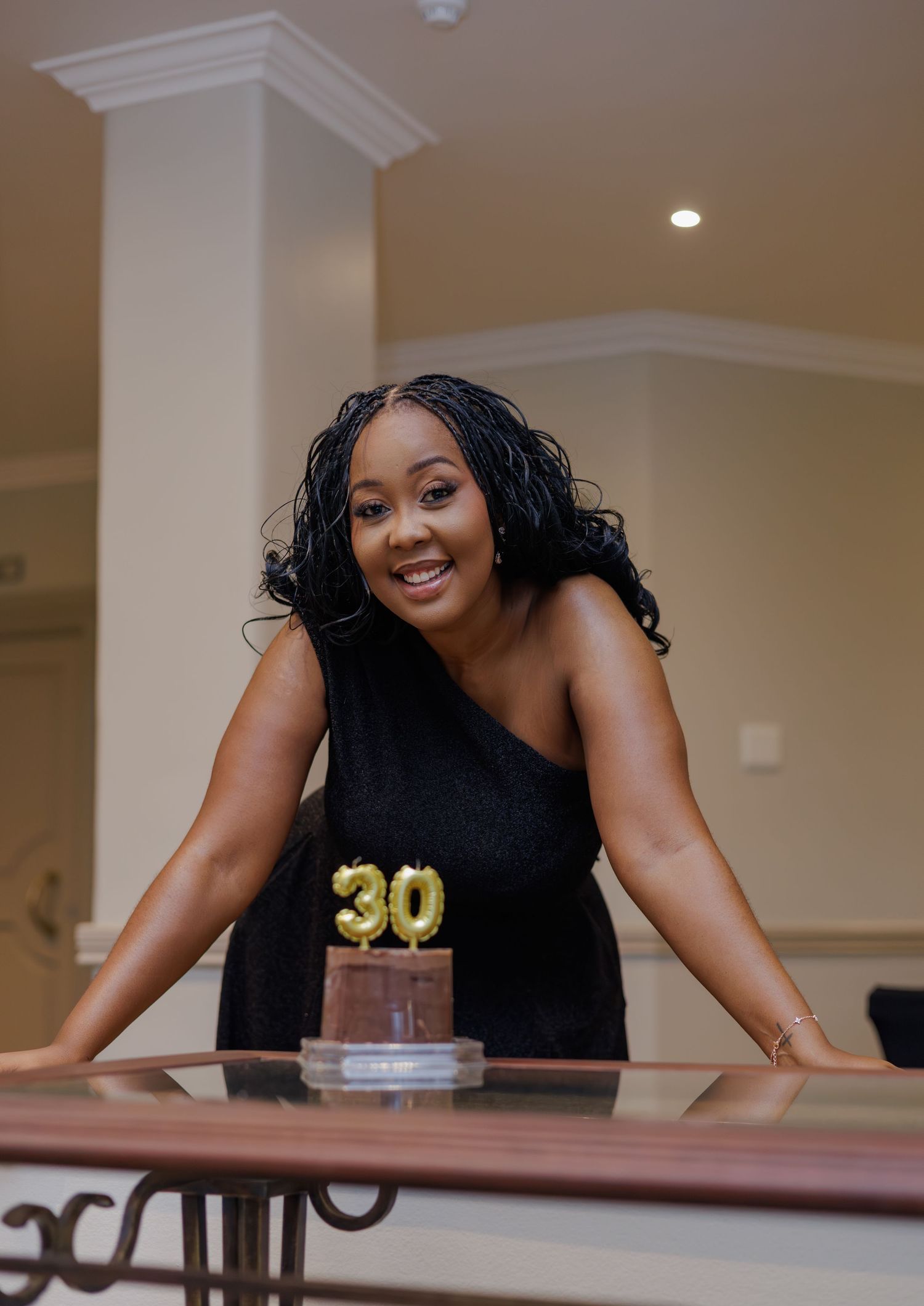 Woman in black dress smiling beside a chocolate cake with gold number 30 candles celebrating her 30th birthday.