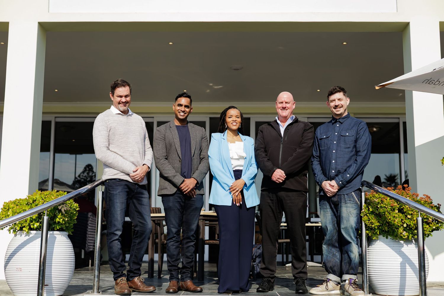 Group of five diverse professionals posing on outdoor steps of a modern white building.