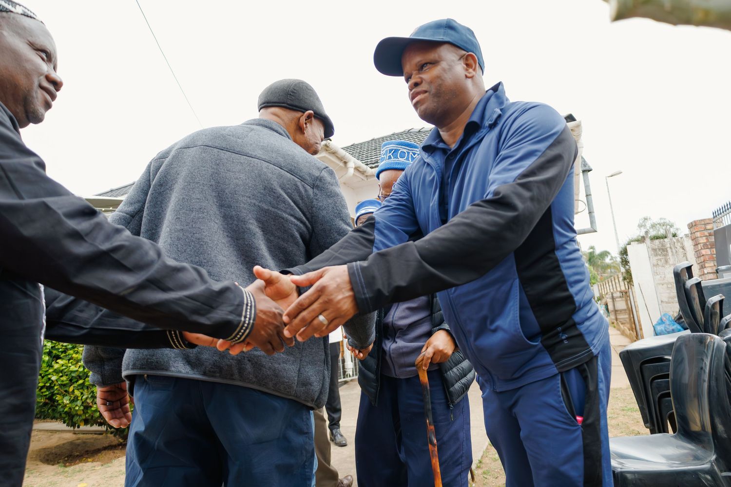 Two men in shake hands warmly at an outdoor community gathering.