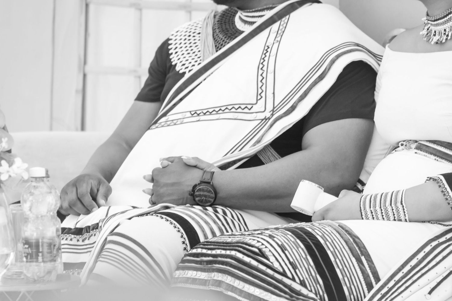 Black and white close-up of a couple in traditional Xhosa attire holding hands at a ceremony.