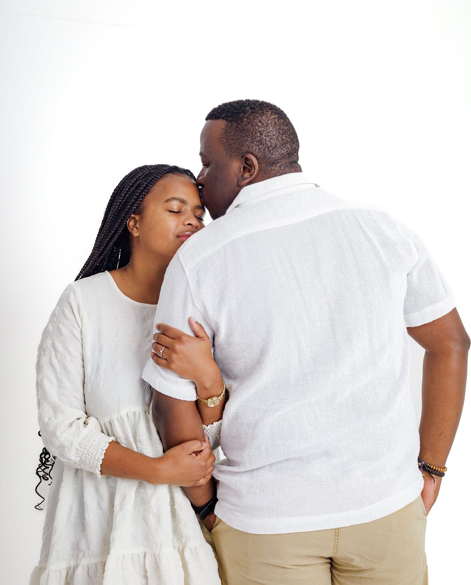 Romantic couple in white outfits sharing a tender kiss against a clean white studio background.