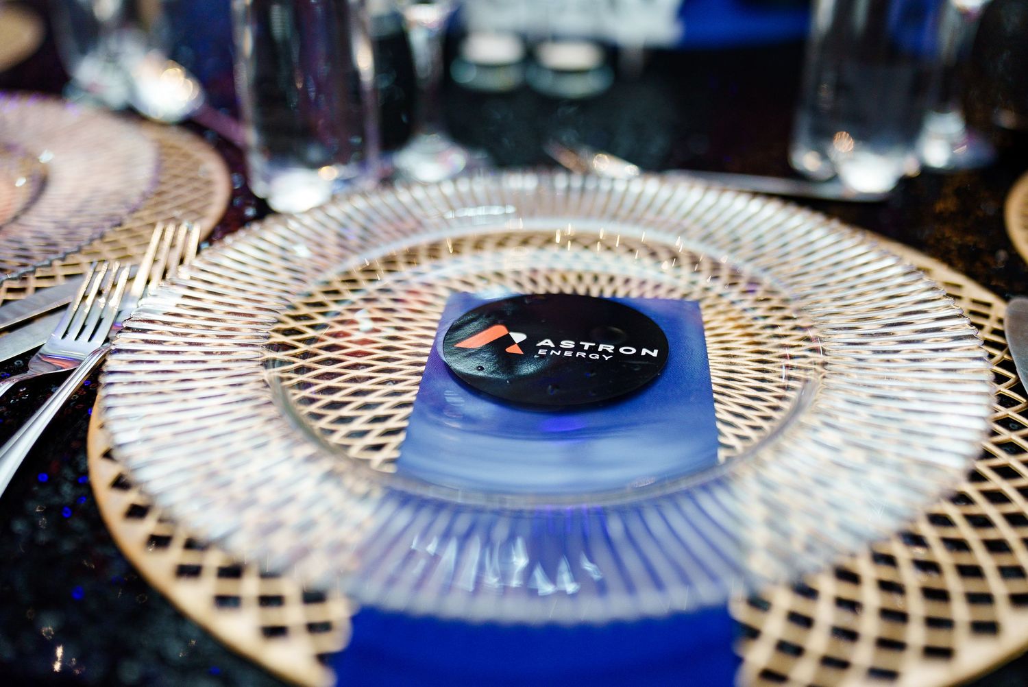 Astron Energy branded napkin on decorative gold plate at formal dinner table setting.