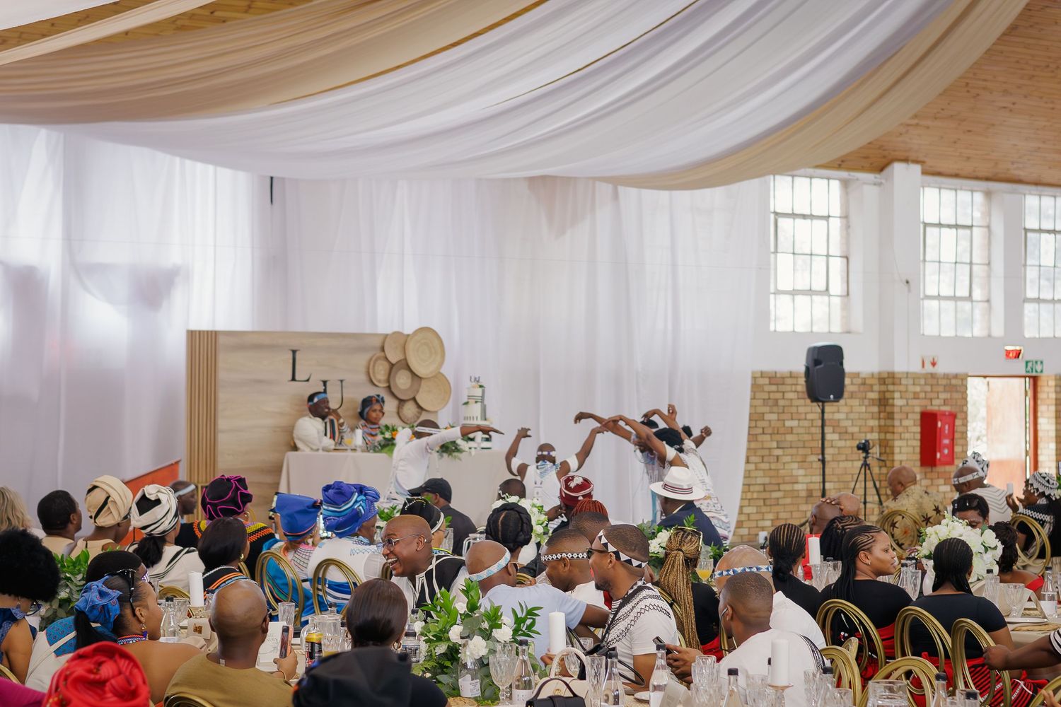Guests seated at tables during a traditional African wedding reception with performers on stage.