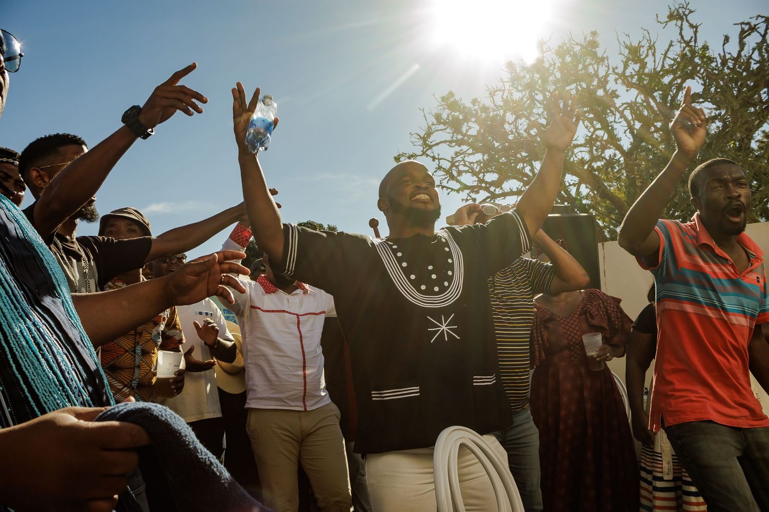 Joyful guests dancing and celebrating outdoors at a vibrant African traditional wedding party in sunlight.