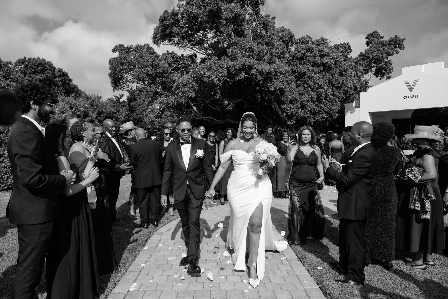 Newlyweds walk through cheering guests outside venue after wedding ceremony.