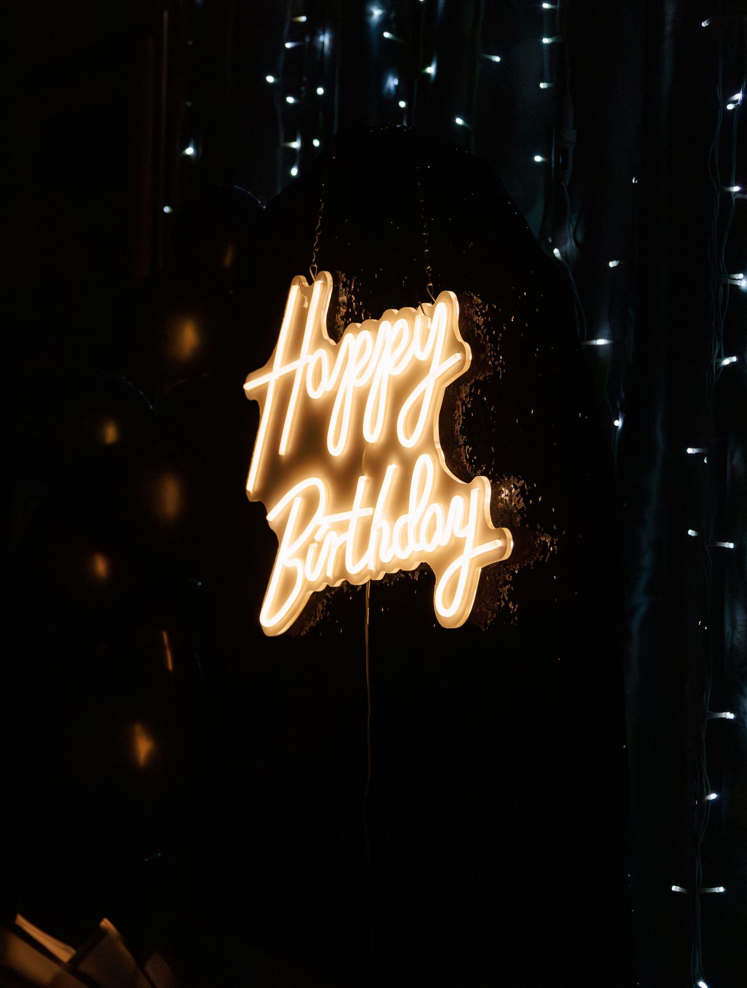 Glowing neon Happy Birthday sign illuminated against dark background with twinkling fairy lights.