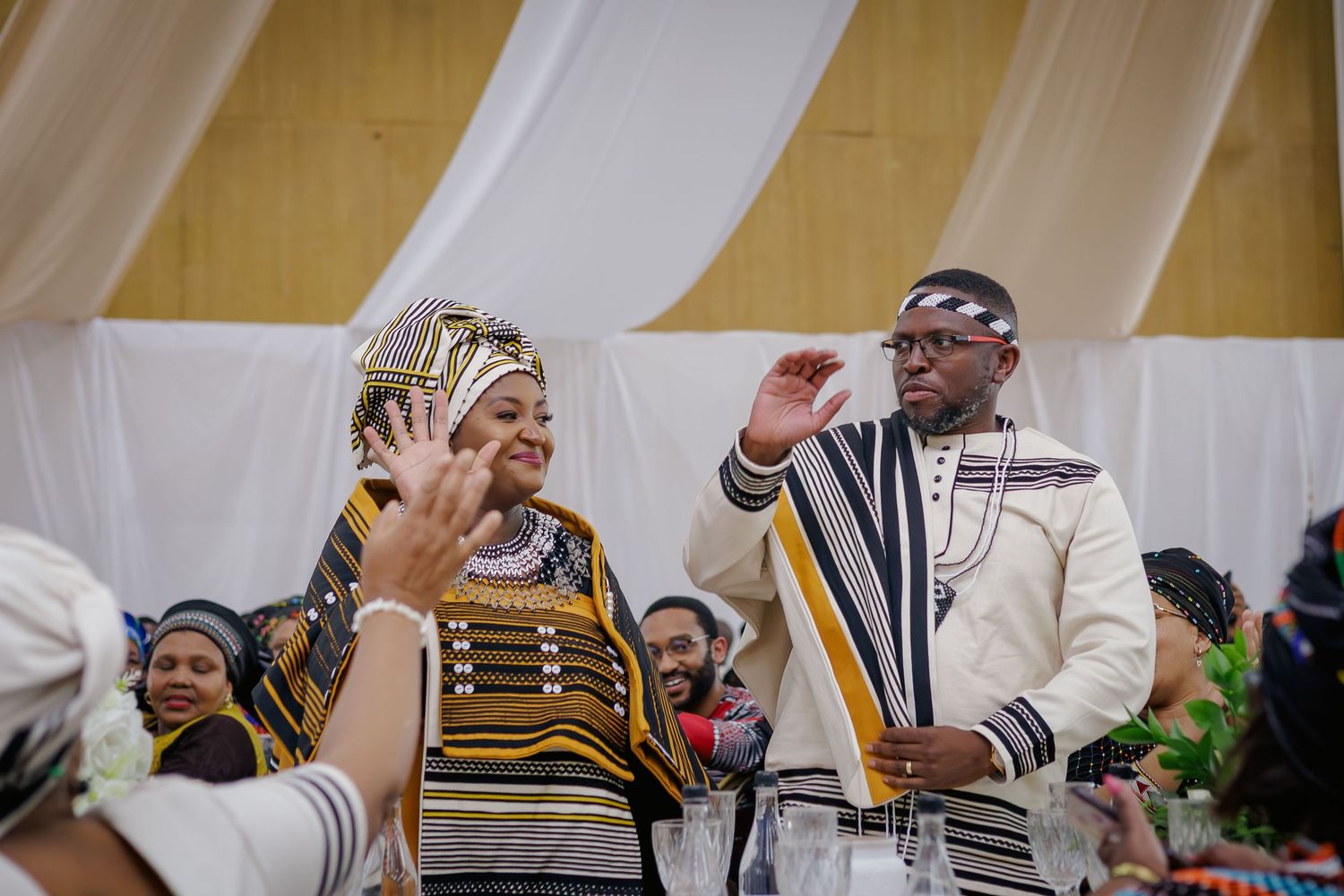 Couple in traditional Xhosa clothing waving at guests during a cultural wedding celebration.