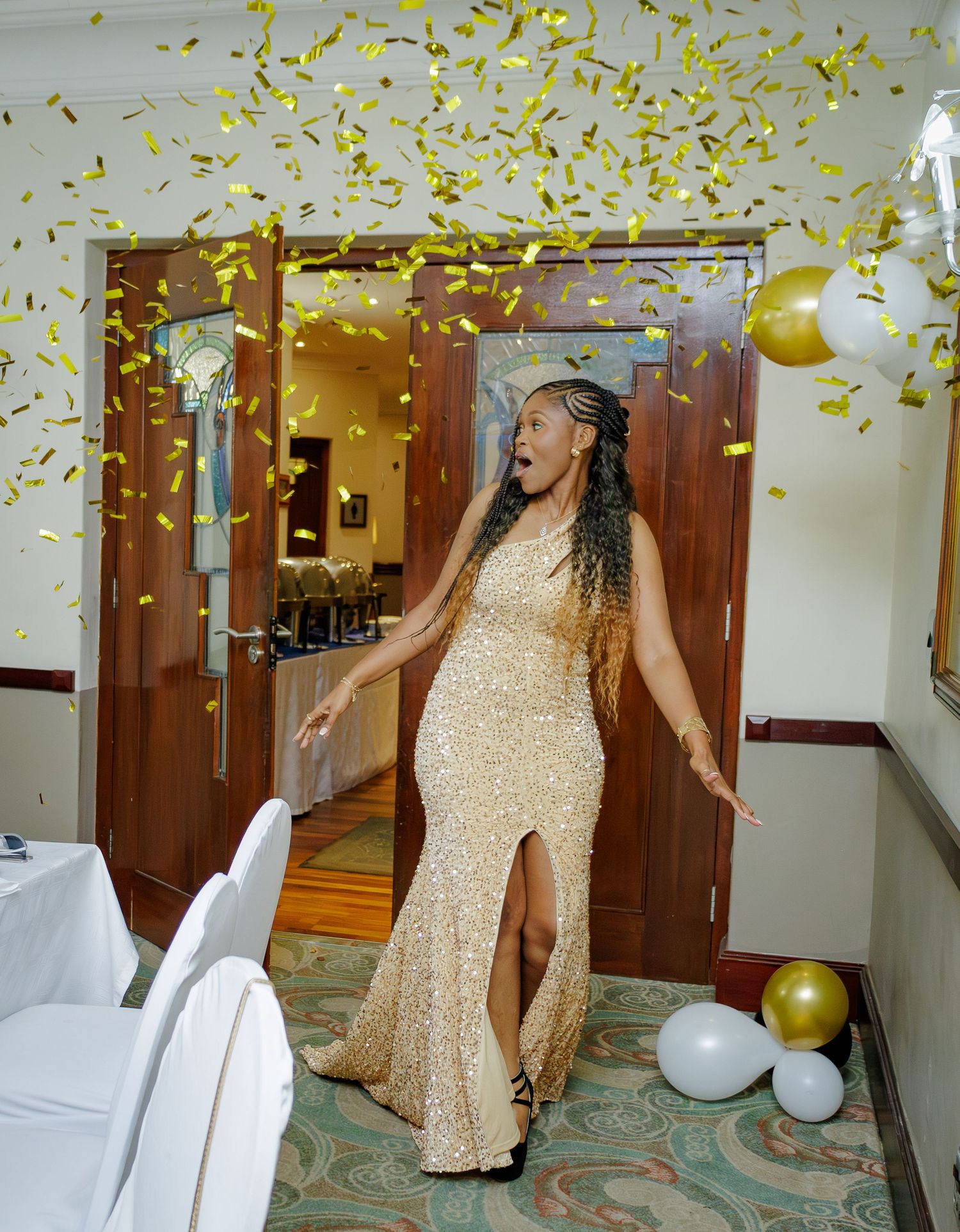 Woman in gold sequin gown celebrating with golden confetti falling at an elegant party venue.