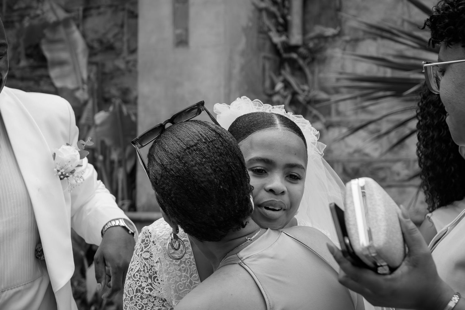 Black and white photo of a bride in a veil receiving warm congratulatory hugs from guests at her wedding.