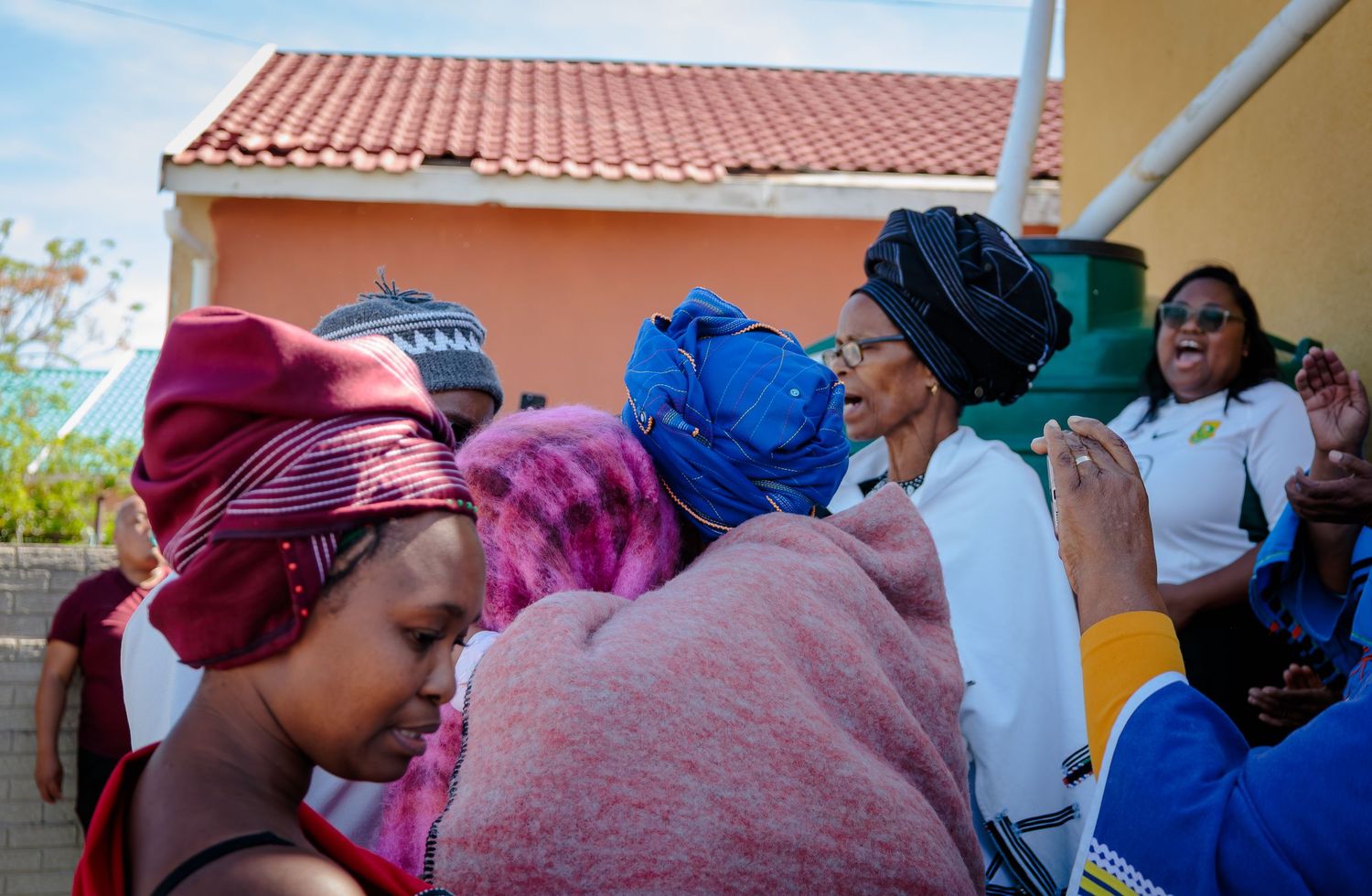 Women in vibrant traditional African headdresses and clothing share joyful moments at a celebration.