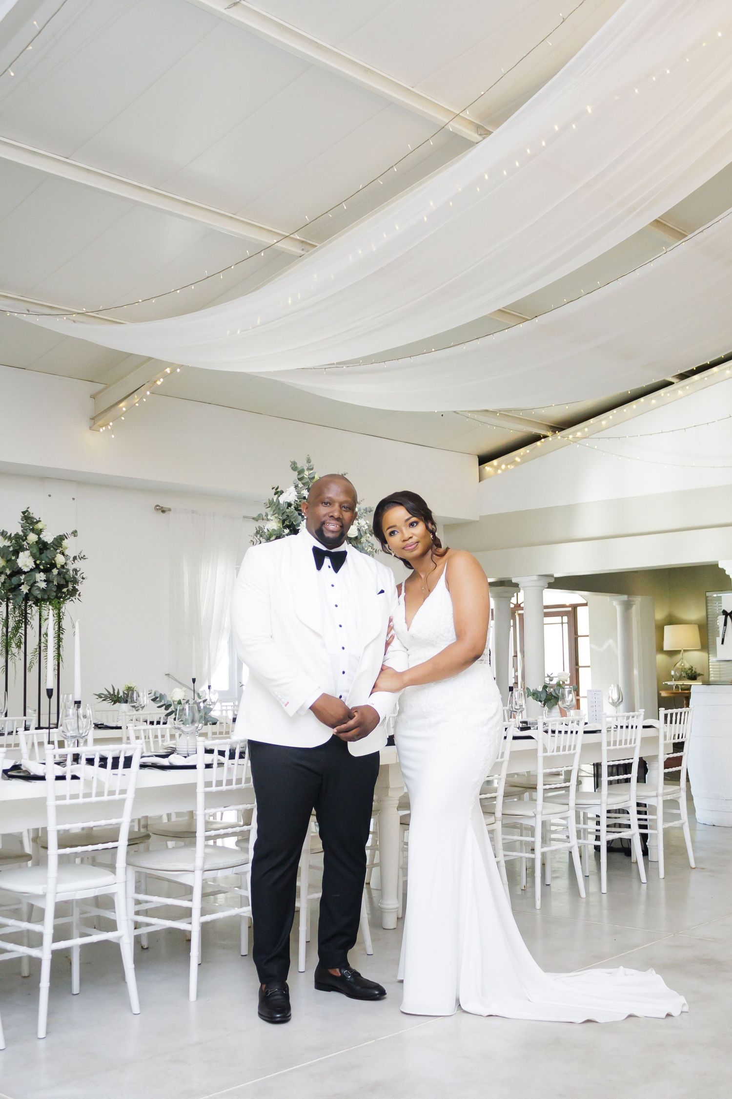 Elegant bride and groom posing in a beautifully decorated white wedding reception venue.