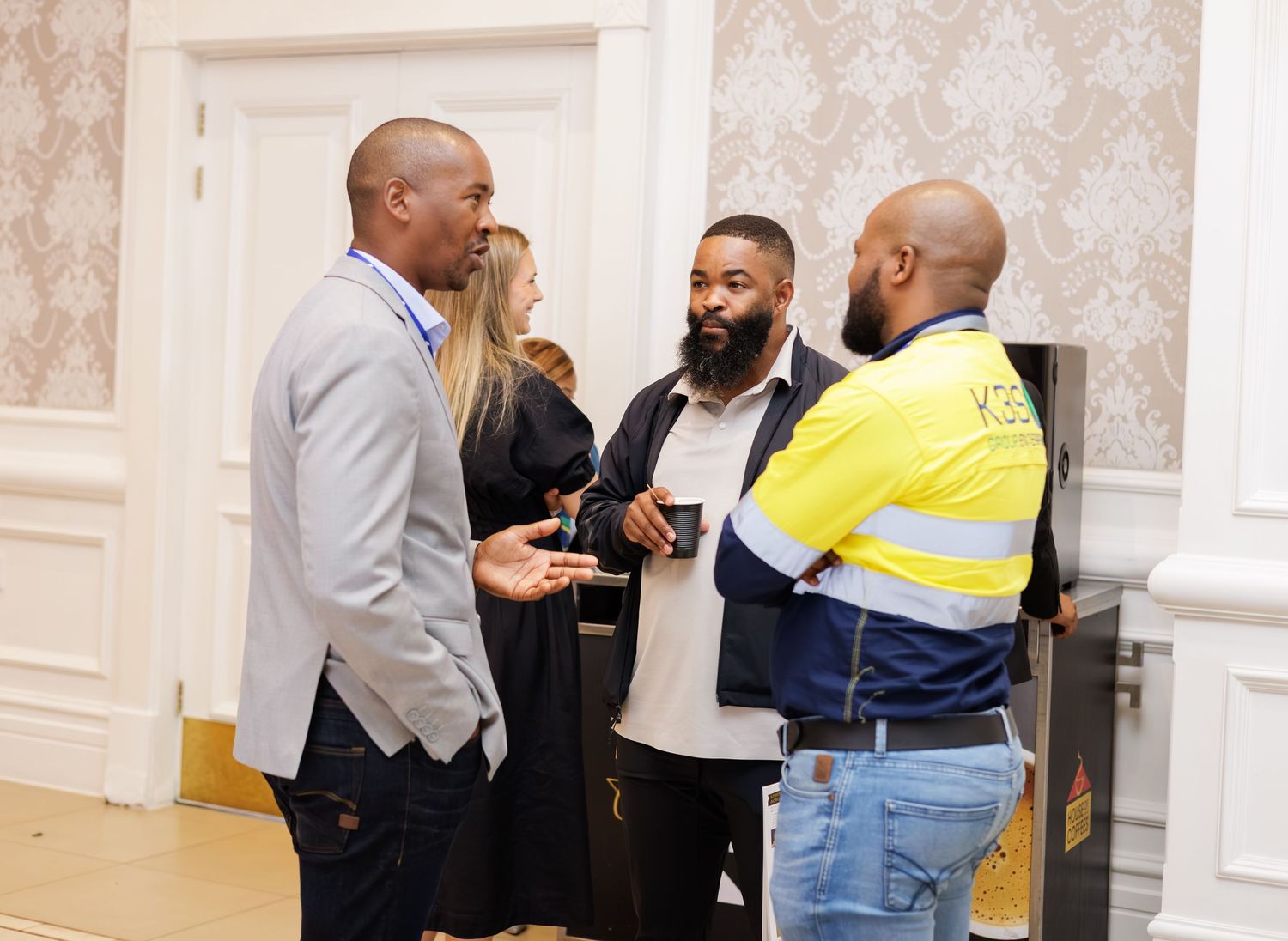 Three professionals networking and conversing at a formal indoor business event.