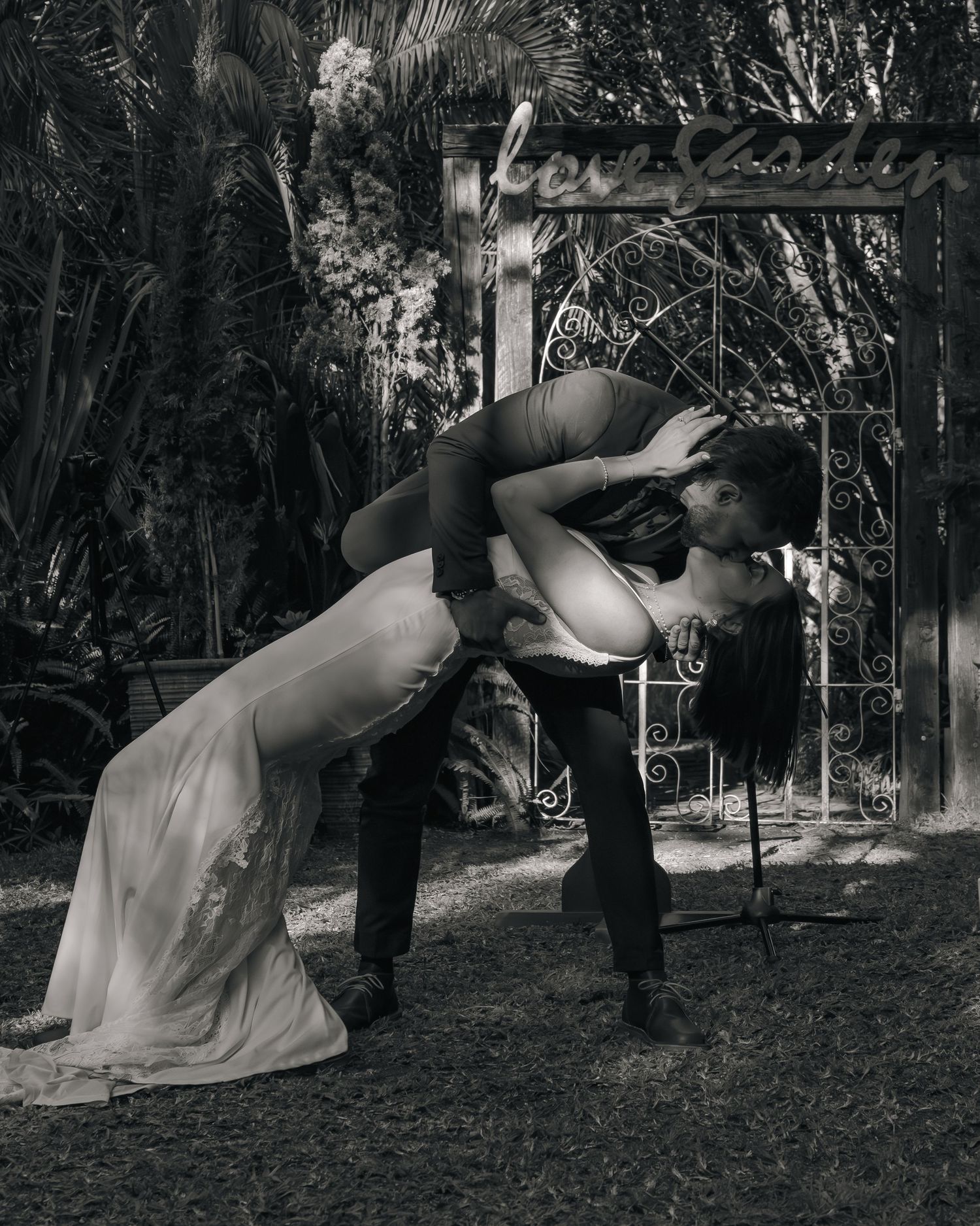 Black and white romantic dip kiss photo of newlyweds in front of an ornate iron garden arch after ceremony.