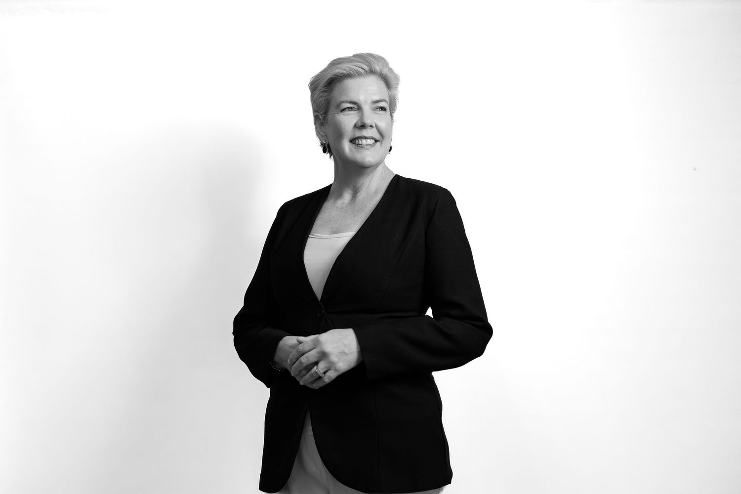 Professional woman in black blazer smiling confidently against white background.