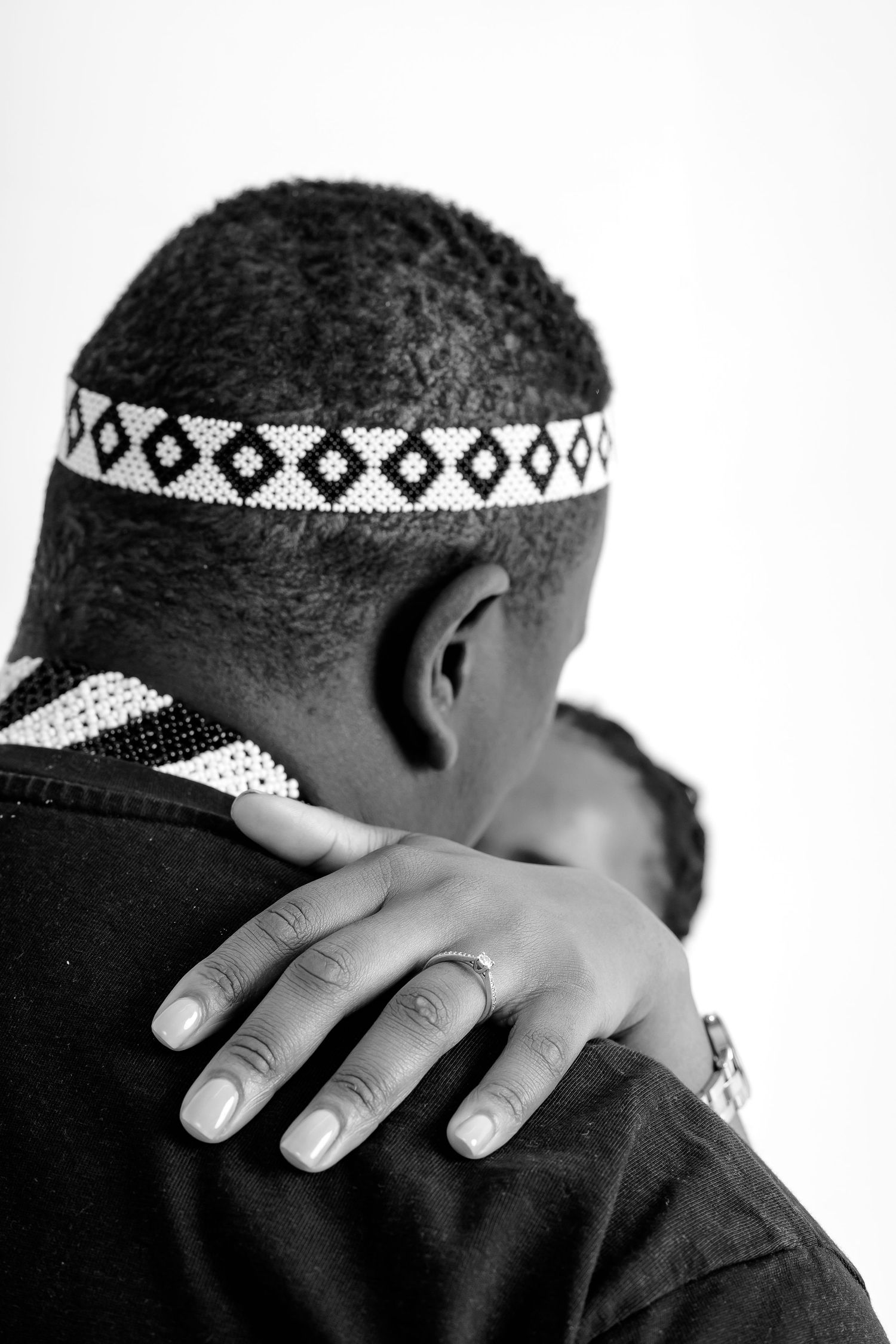 Black and white close-up of man wearing beaded African headband being embraced by partner.